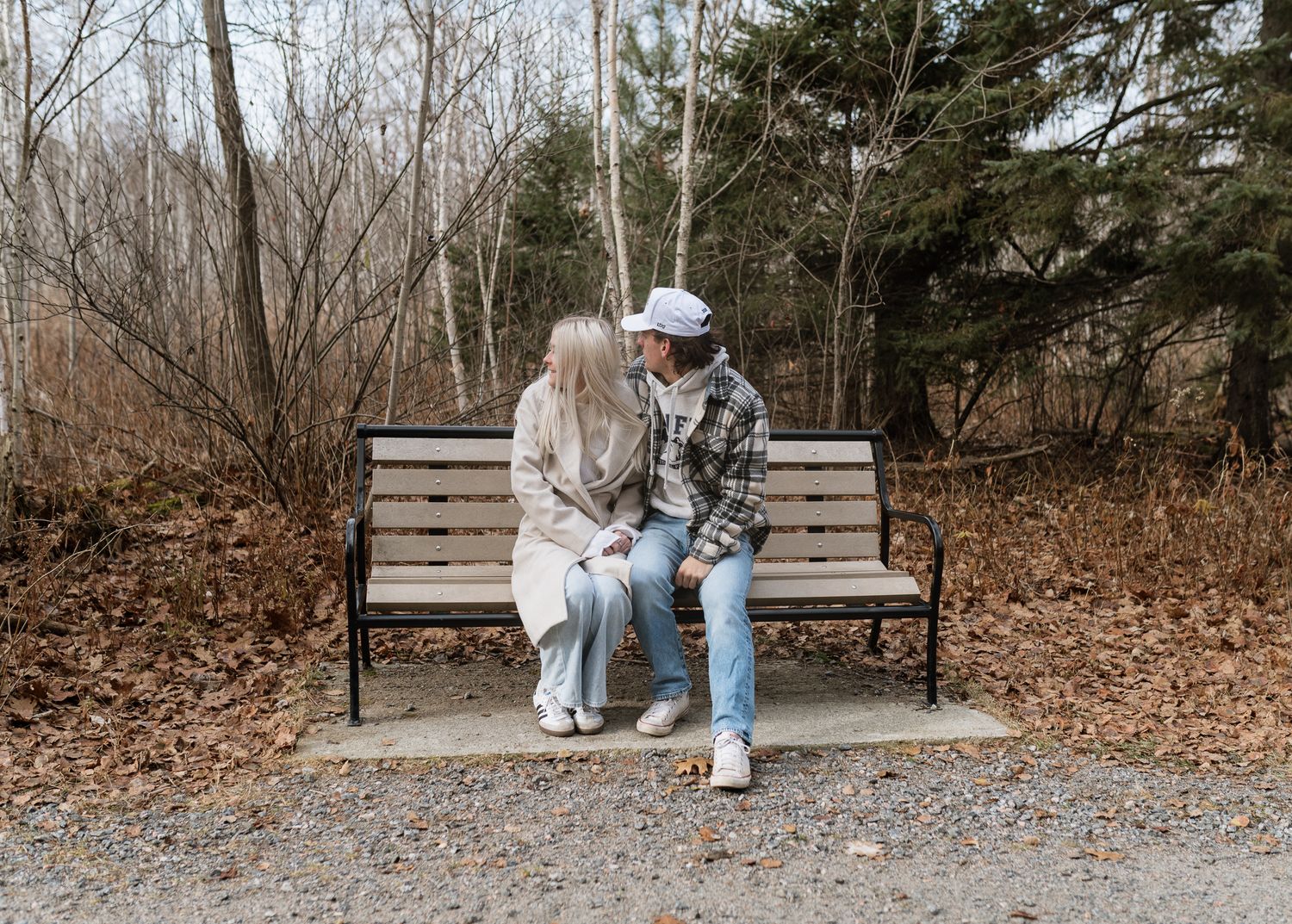 A couple sitting close together on a wooden park bench surrounded by autumn foliage.