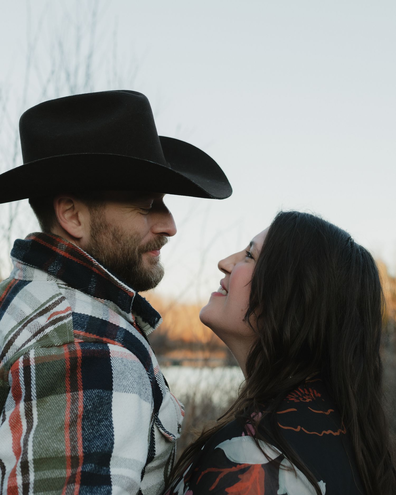 A romantic couple in western wear share an intimate moment against a winter sky backdrop.