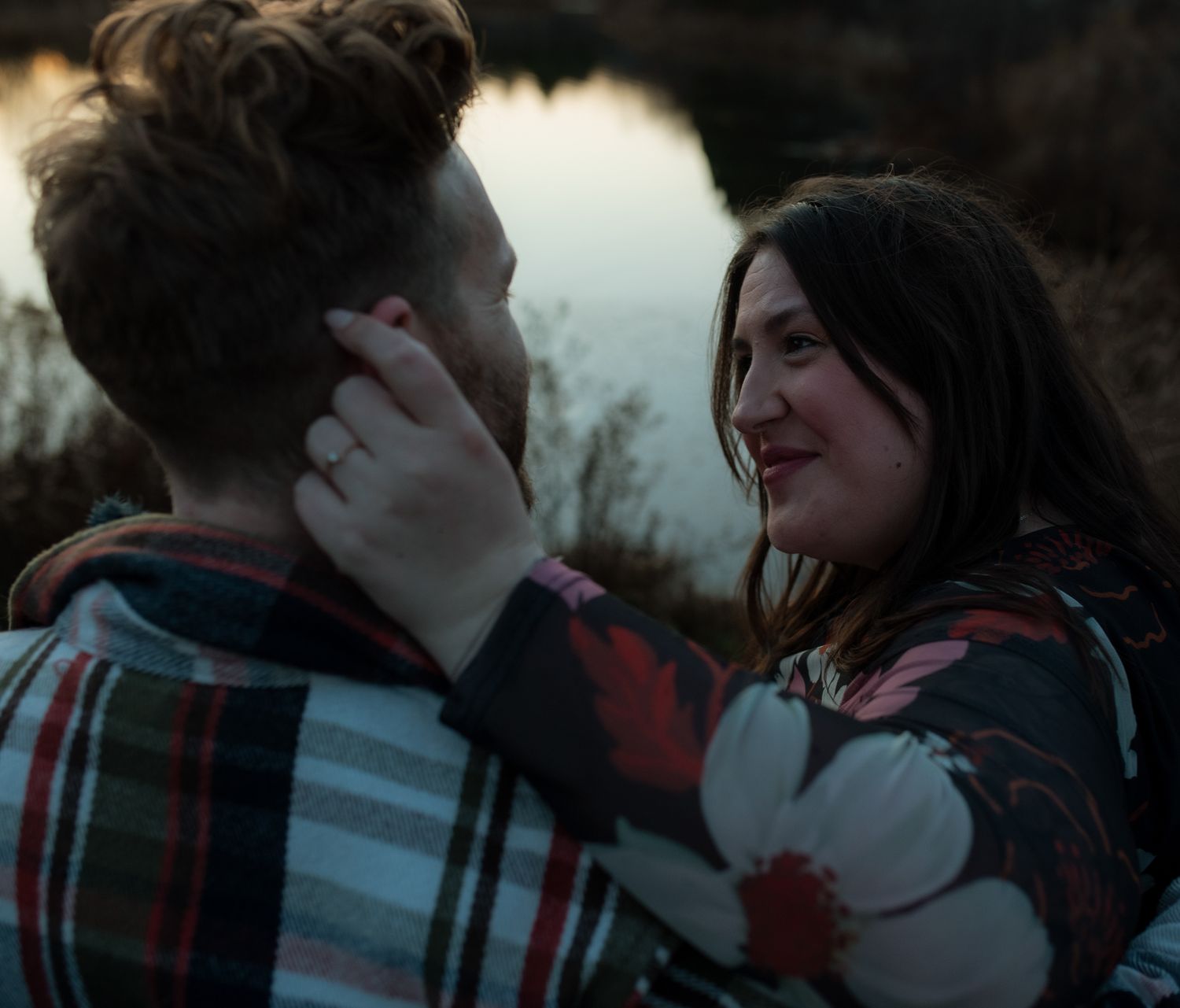 A couple in a plaid shirt share an intimate moment outdoors during sunset.
