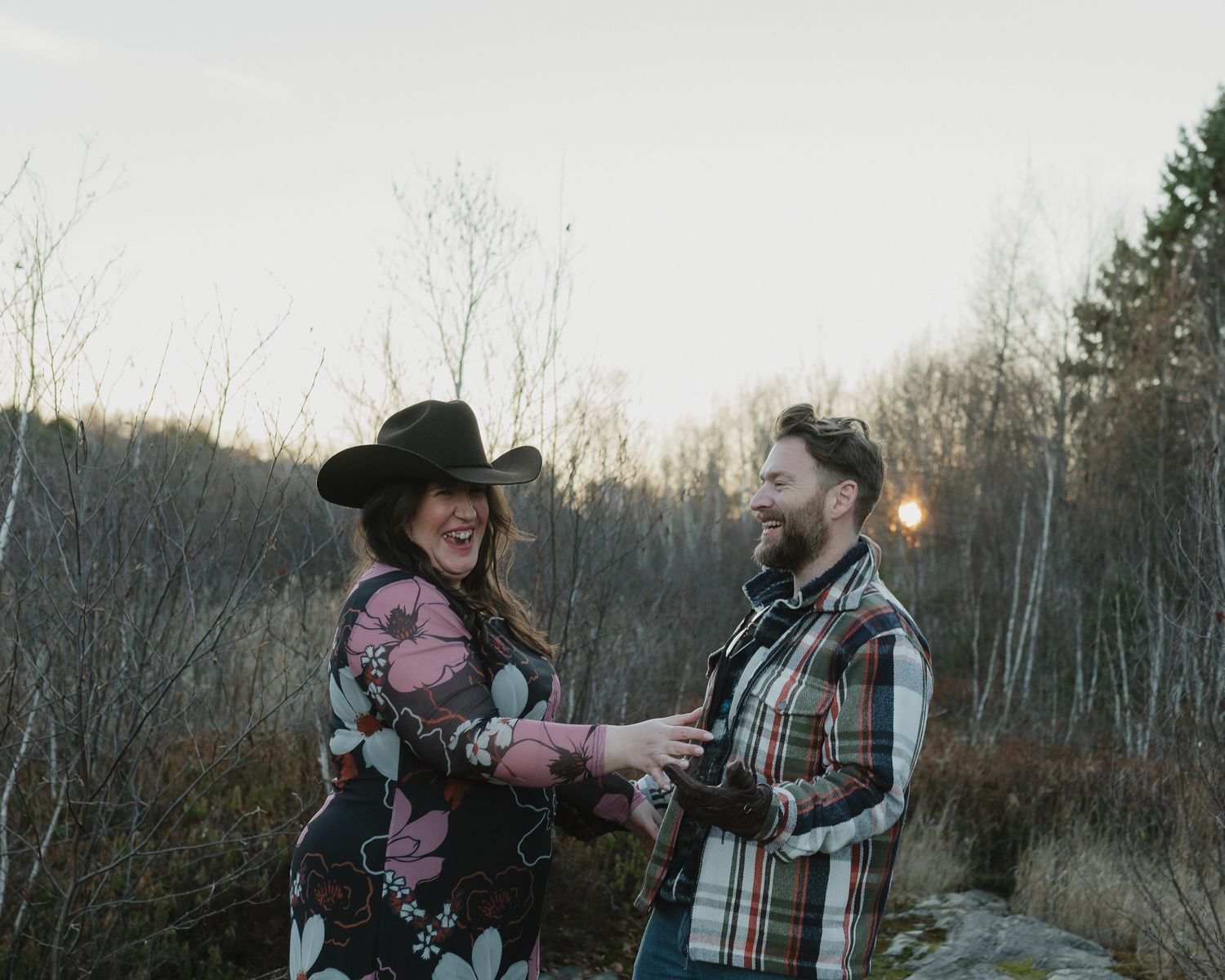 A couple embraces in a romantic moment outdoors during sunset with trees in the background.
