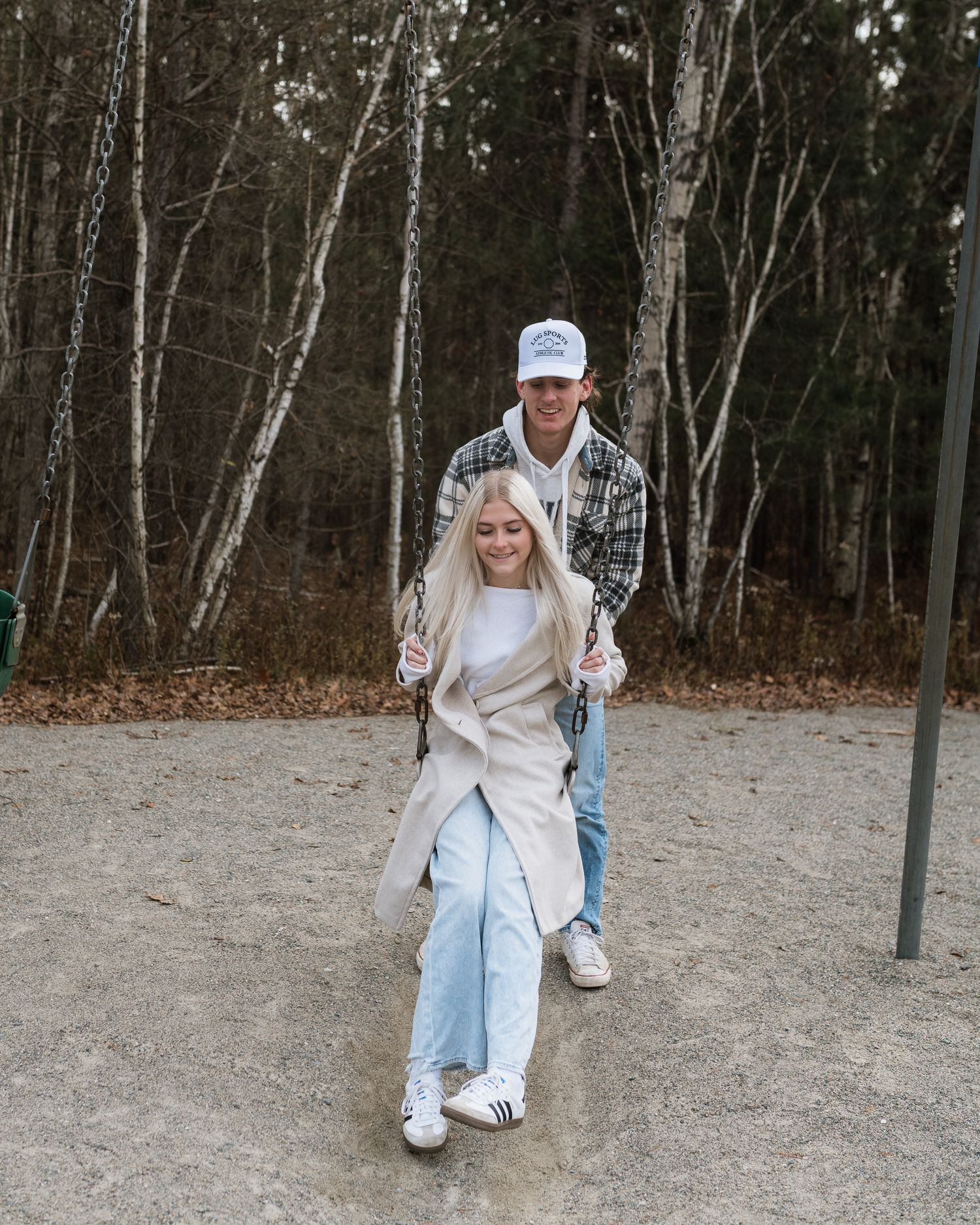A couple walking together at an outdoor playground, man in plaid shirt and cap with blonde woman in beige coat.