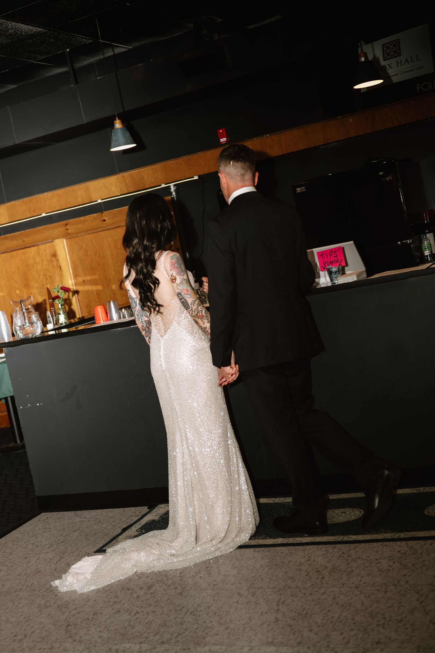 Bride and groom holding hands at the bar, bride wearing a sequined gown with long sleeves and train.