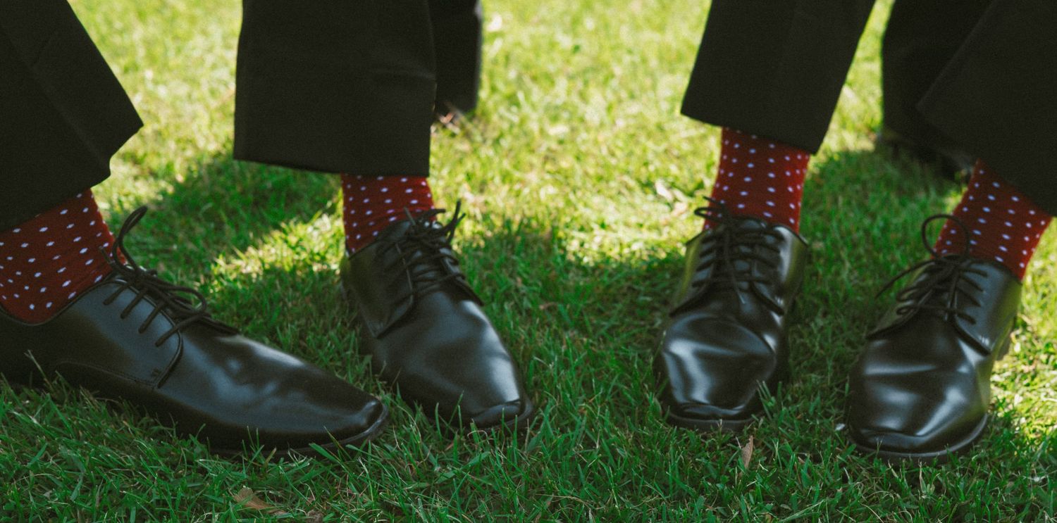 Dress shoes and boots lined up on grass during an outdoor wedding ceremony.