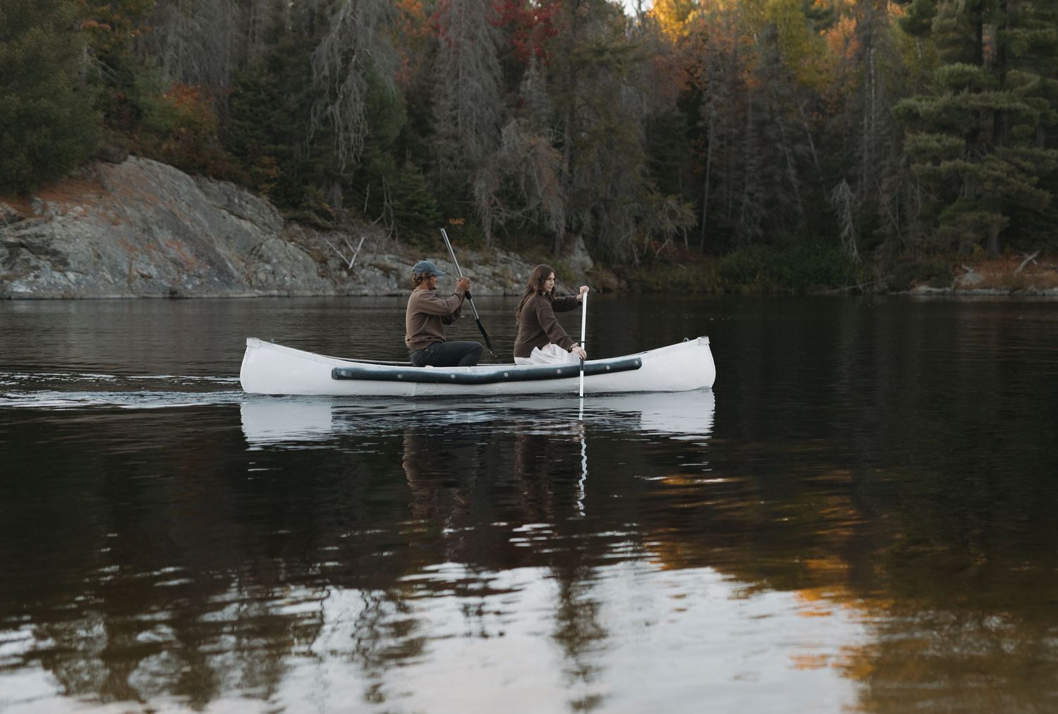 A peaceful lake scene with a white canoe against a backdrop of fall foliage and rocky cliffs.