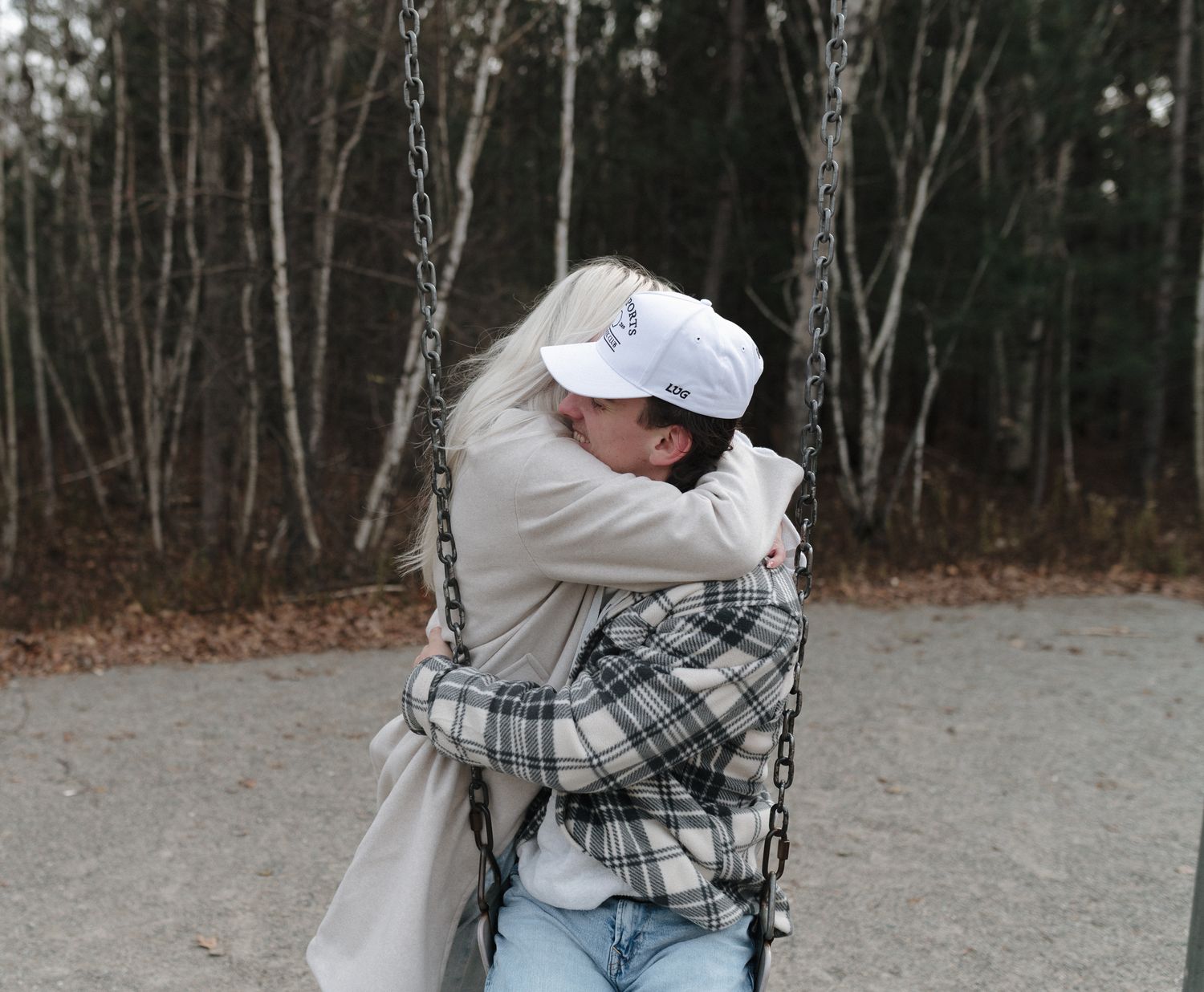 Two people sharing a warm hug on a swing in a wooded park during autumn.