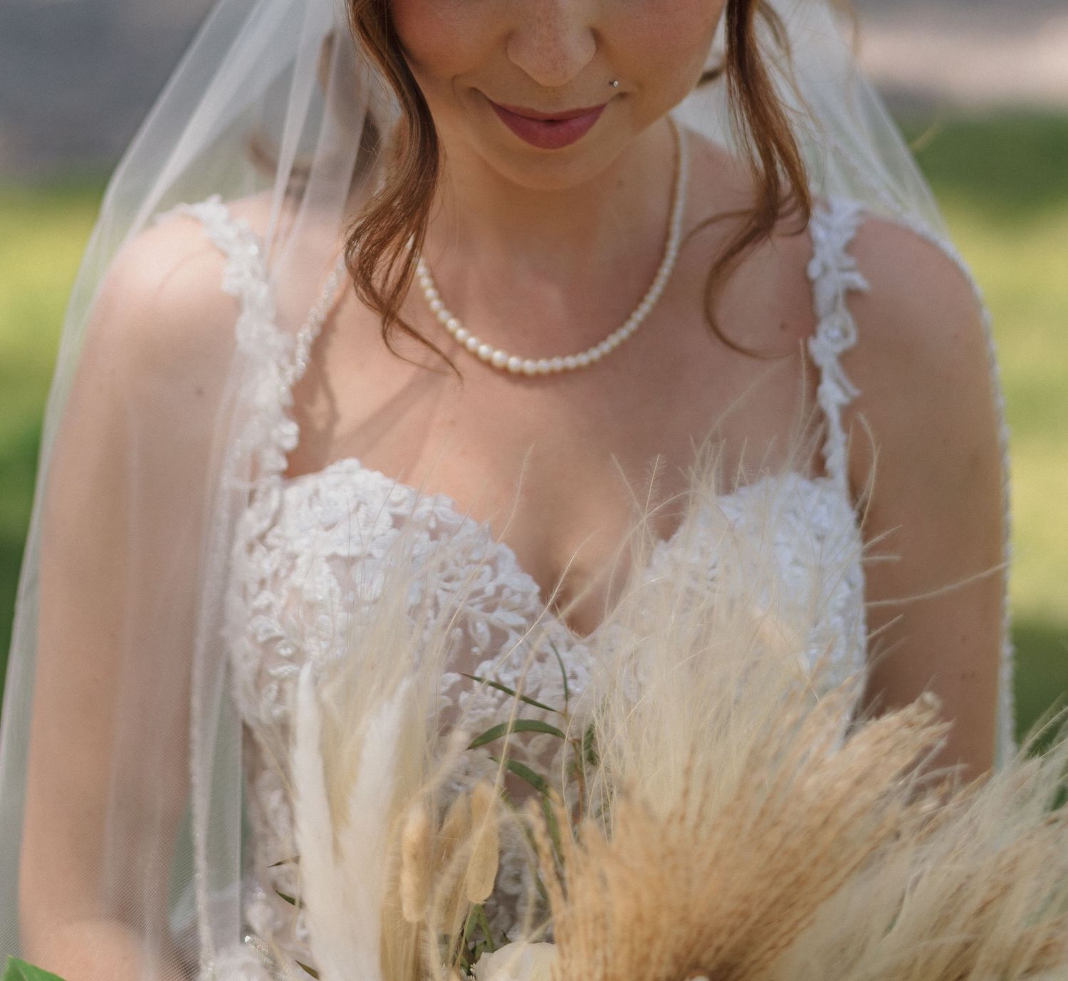 Bride holding rustic bouquet with pampas grass and dried flowers against outdoor backdrop.