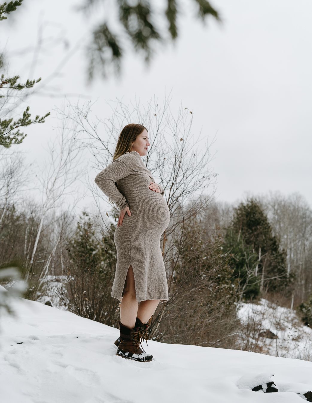 Winter maternity photos taken in a snowy landscape with bare trees.