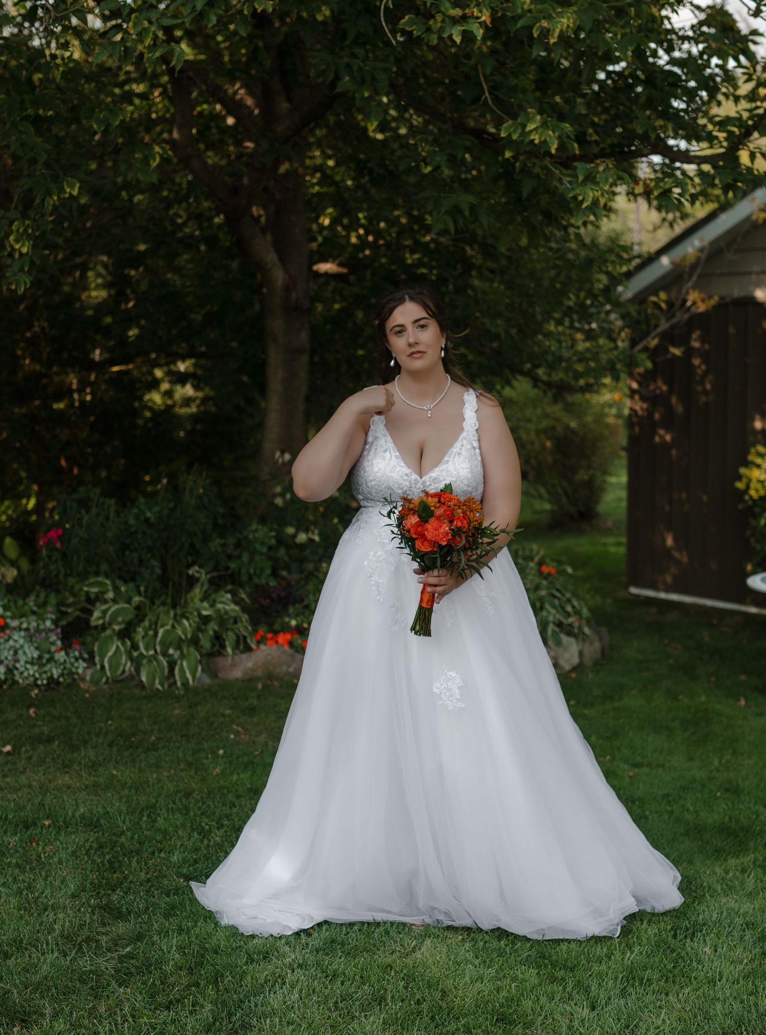 Bride in lace v-neck gown holds vibrant orange bouquet in garden setting.