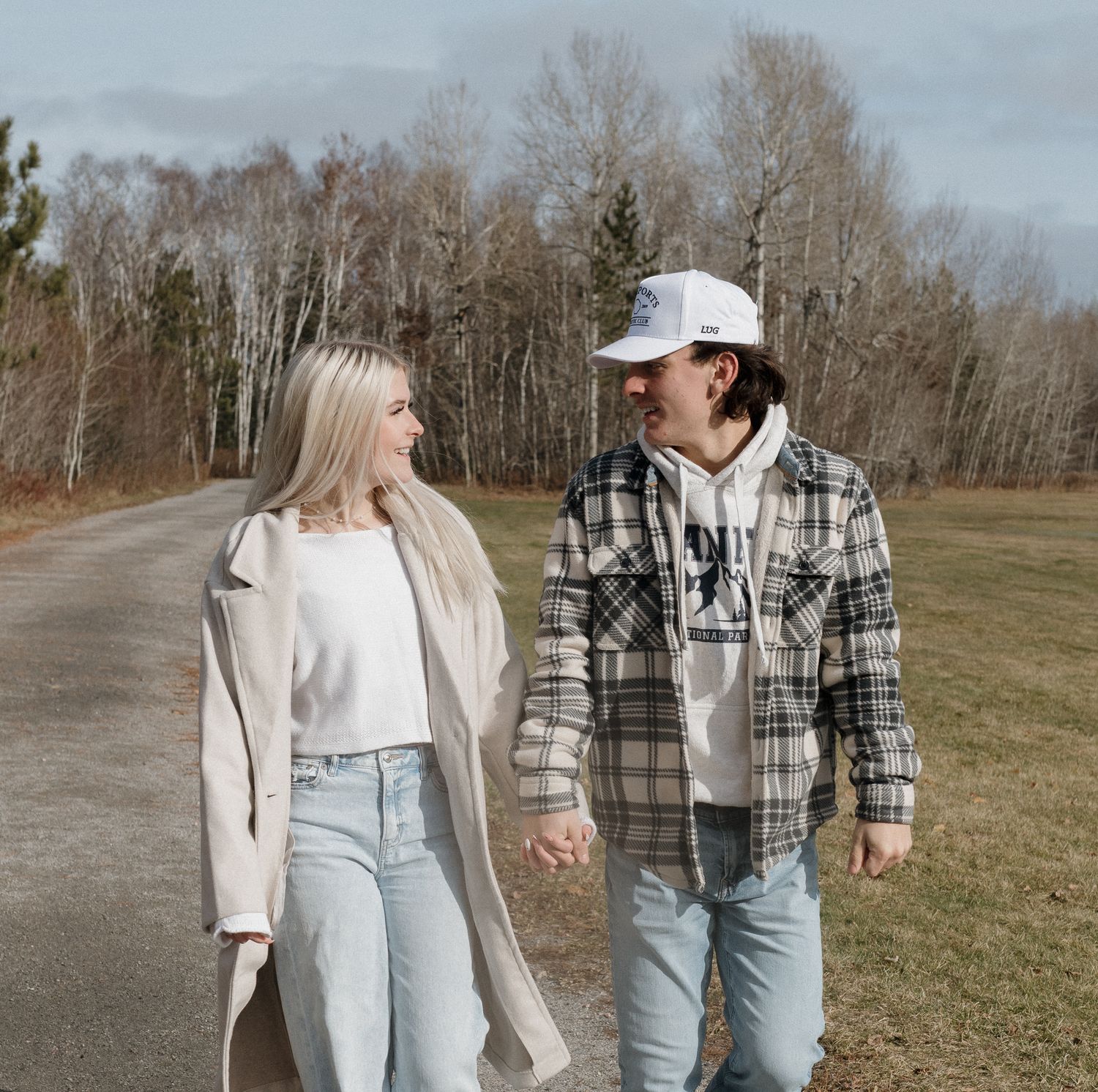 Happy young couple walking hand in hand on open path with bare trees in background.