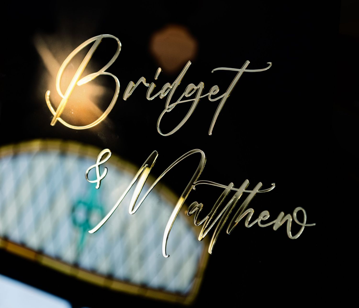 Gold script wedding signage reading Bridget and Matthew on a dark elegant background.
