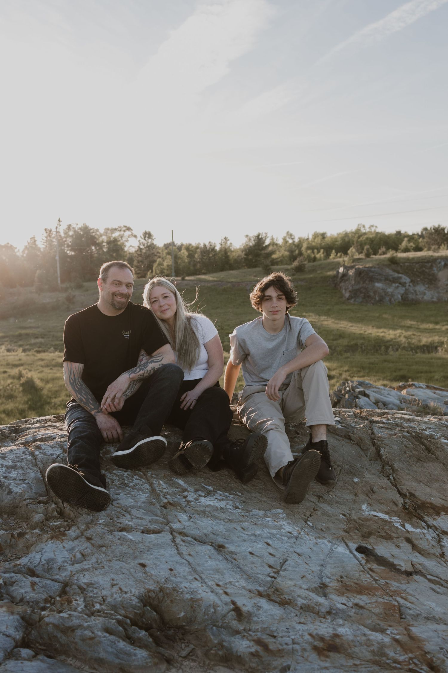 Family of three sitting on rocky outcrop at golden hour with green landscape behind them.