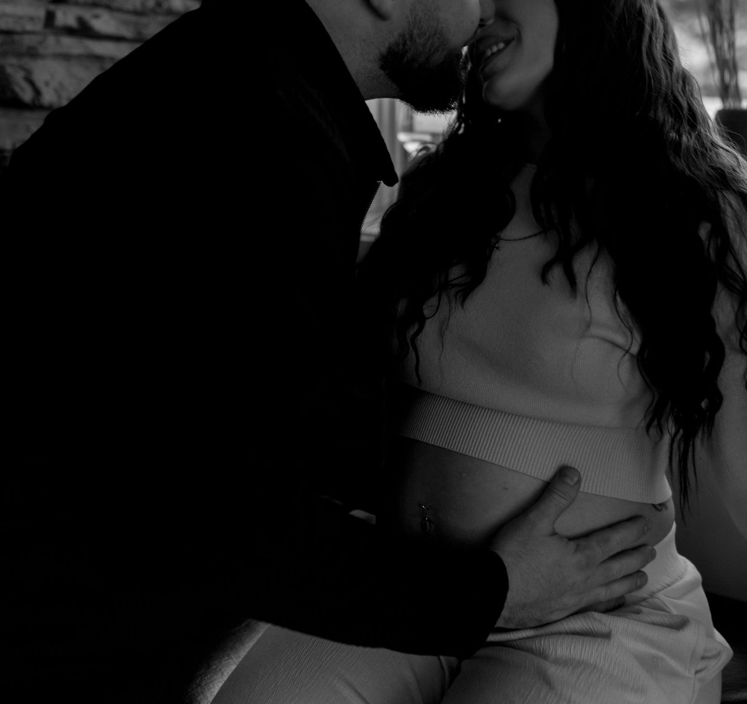 Expectant couple shares an intimate embrace, partner kissing pregnant woman's head while cradling her baby bump.