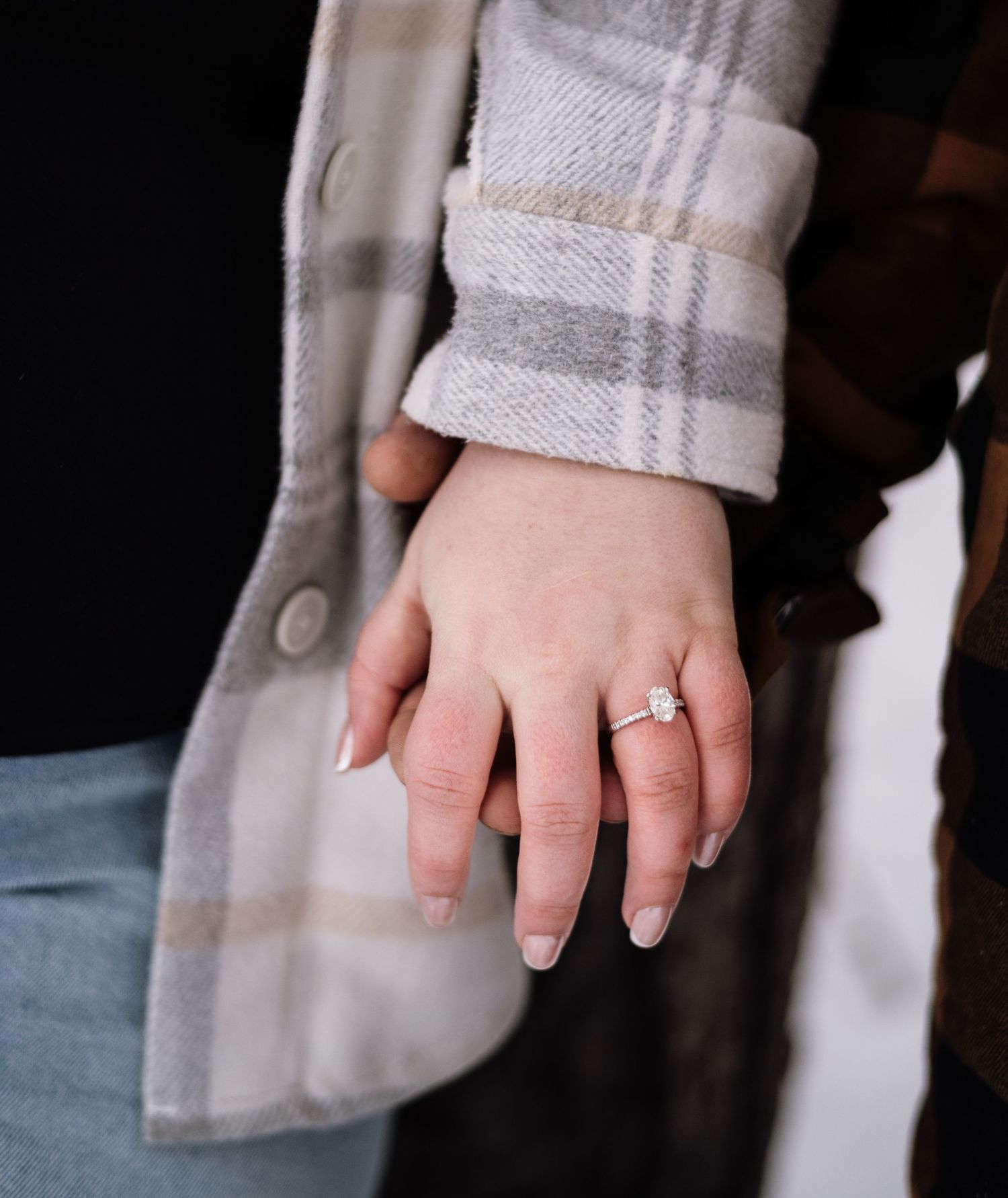 Close-up of a hand wearing a stunning emerald-cut diamond engagement ring, with a plaid jacket sleeve in the background.