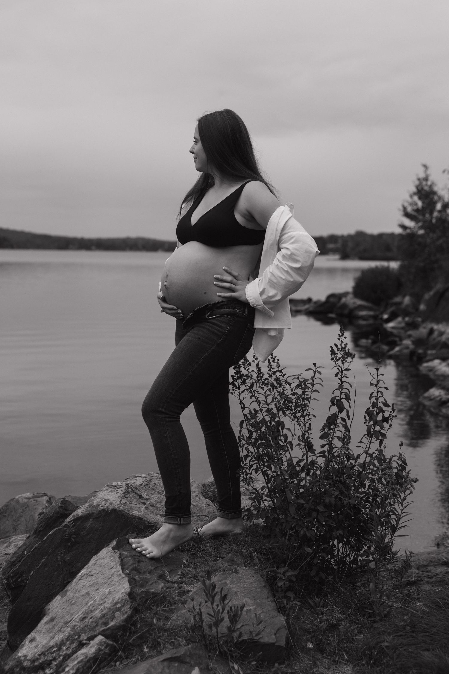 Five artistic black and white photos capturing poses on rocky coastal terrain overlooking a serene waterfront.
