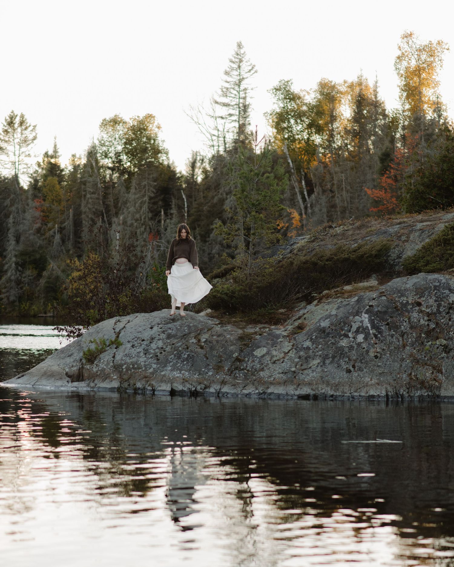 Dramatic rocky shoreline with evergreen forest backdrop captured during golden hour.