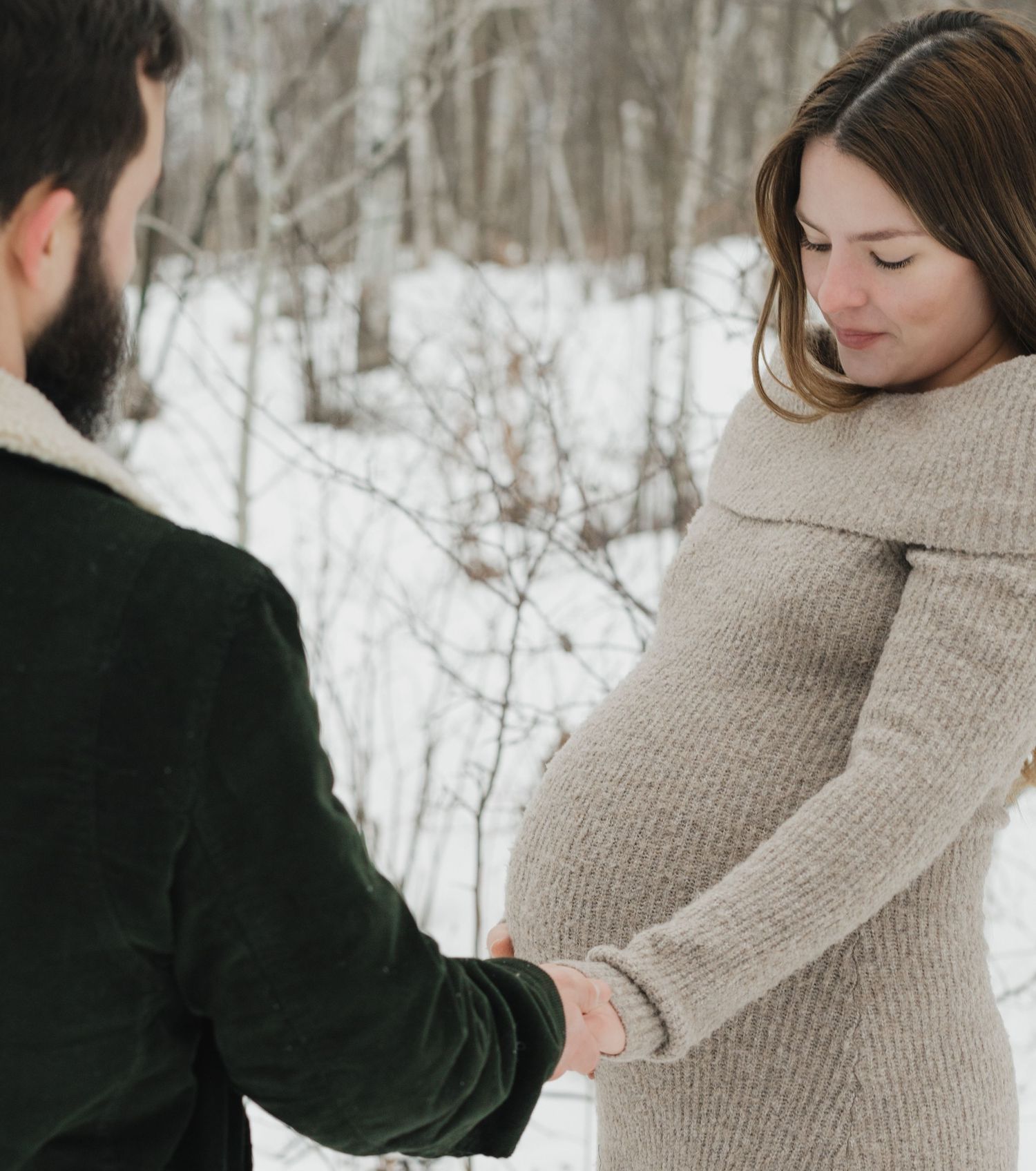 Winter maternity photoshoot with couple in snow covered forest setting.