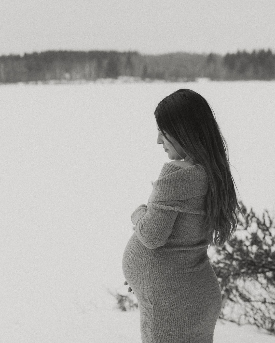 Winter maternity photography session with snow covered landscape in background.