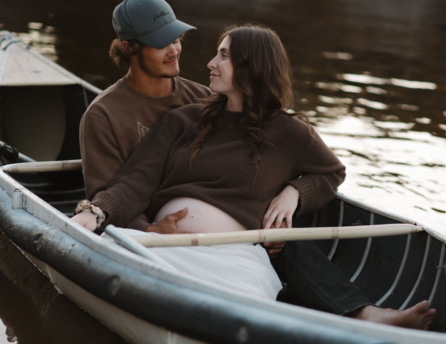 Two people sitting close together in a wooden canoe on peaceful waters.