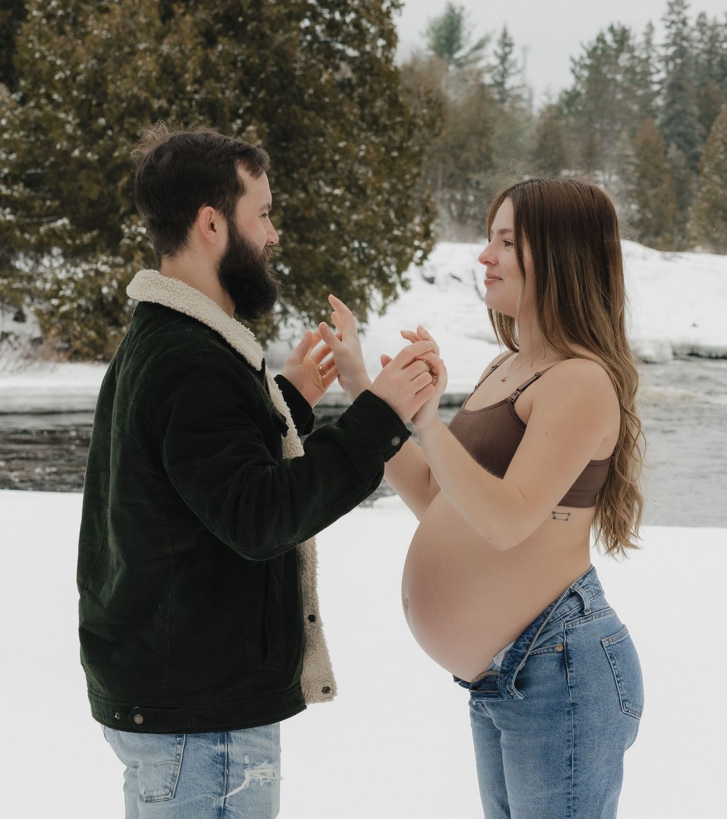 A couple holds hands in the snow during a winter maternity photoshoot.