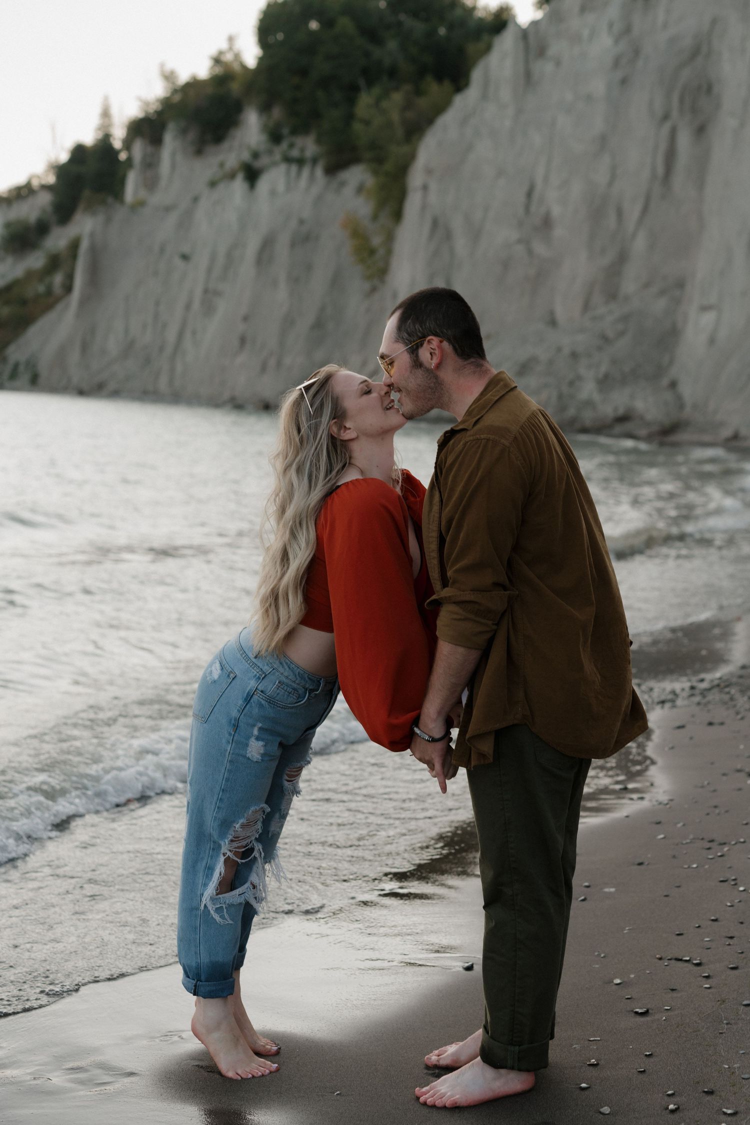 A romantic beach photoshoot with a couple in casual attire against white cliffs at sunset.