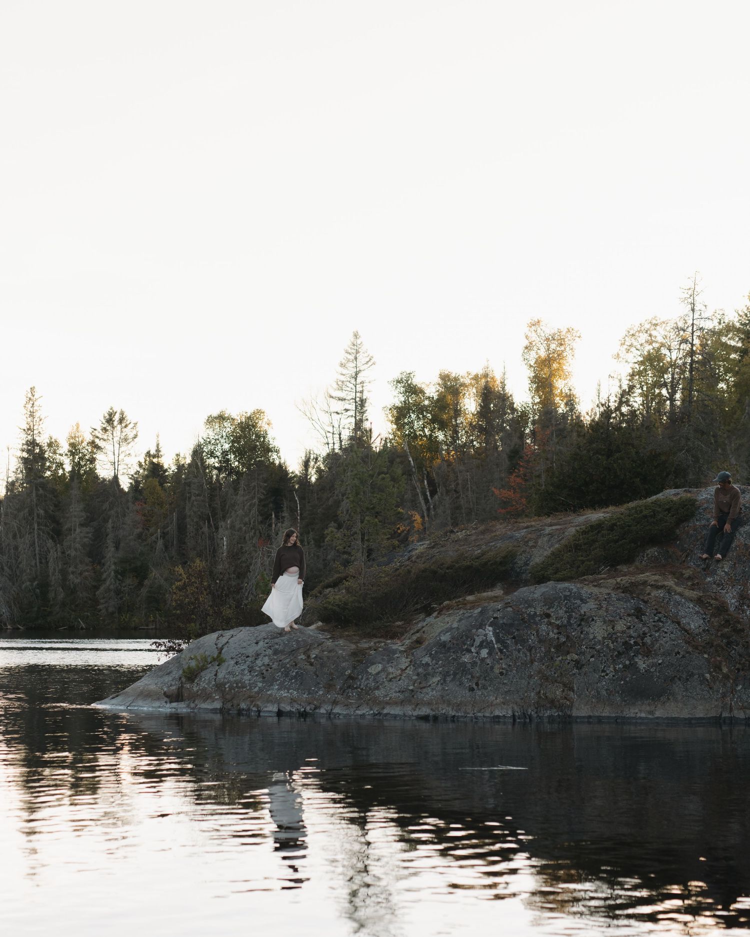 Peaceful wilderness scene with rocky outcrops and forest reflecting in still water.