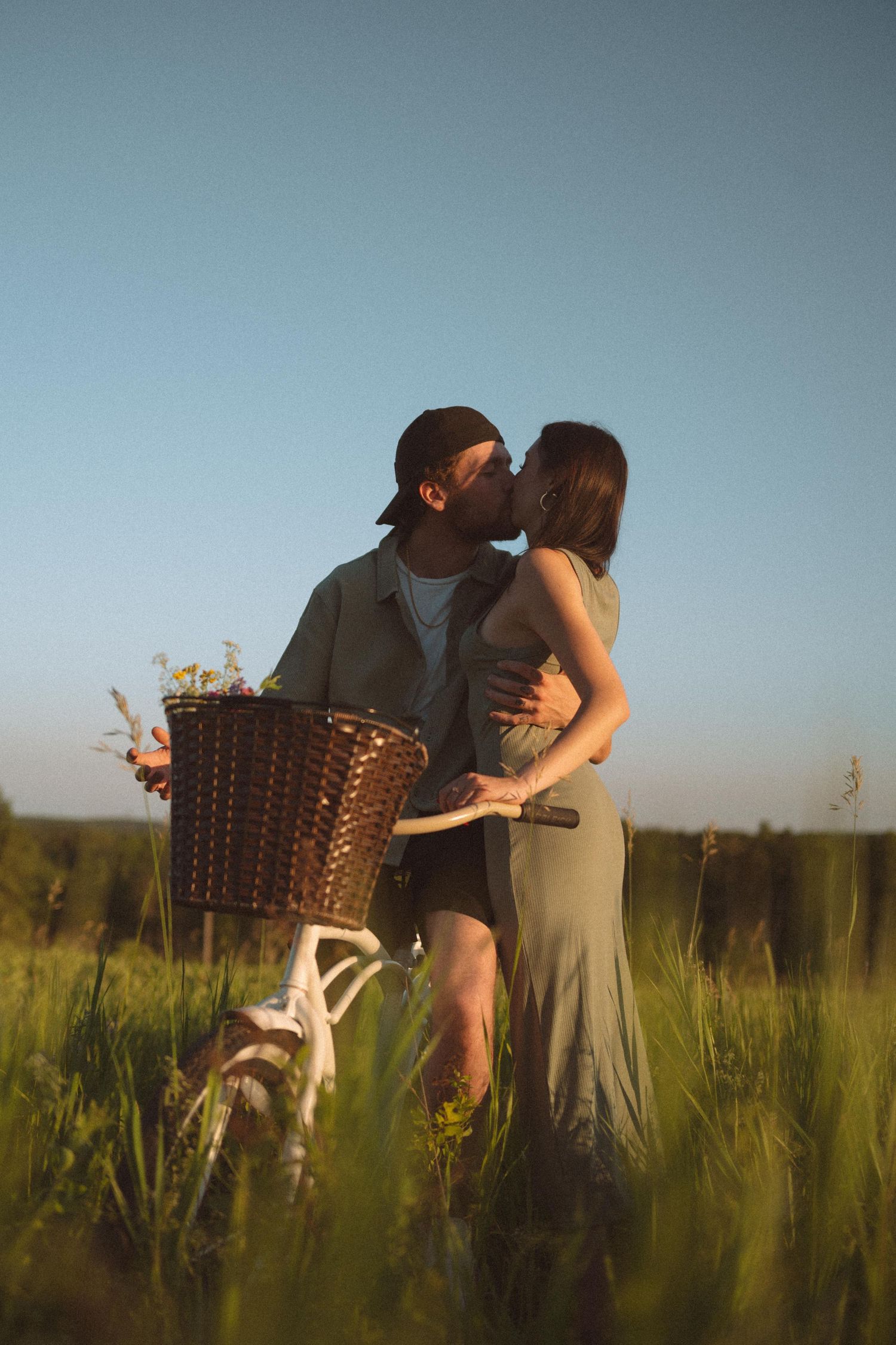 A romantic couple embraces in a sunlit field of tall grass during golden hour.