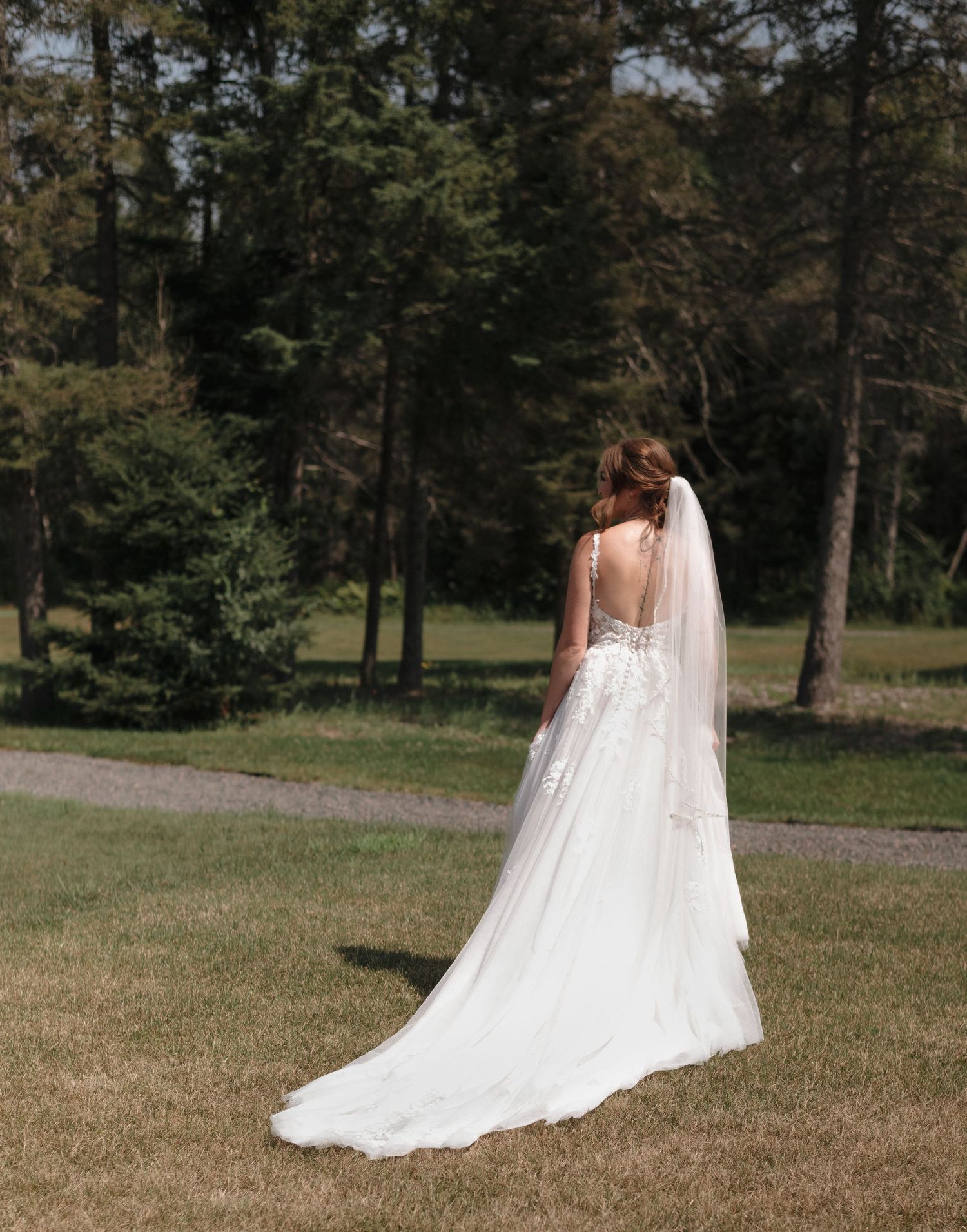 Wedding dress with sheer back detail and flowing train photographed in an outdoor setting.