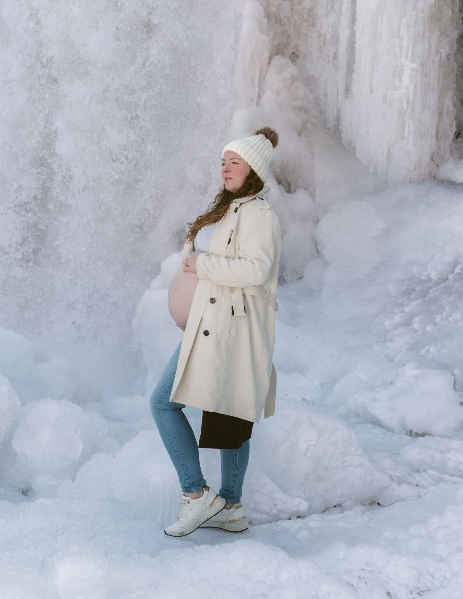 Person in winter attire crouches near a snowy white wall.