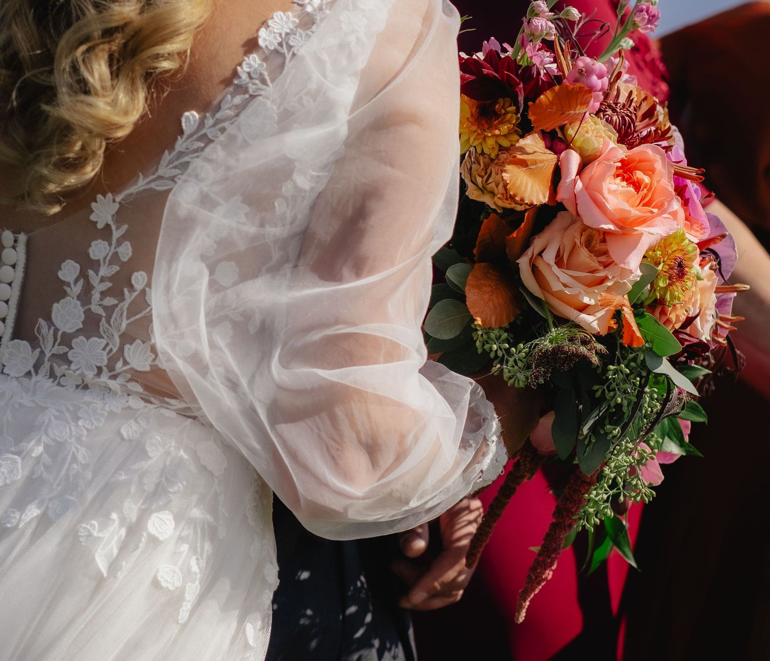 Close-up of intricate lace wedding dress details with colorful floral bouquet.