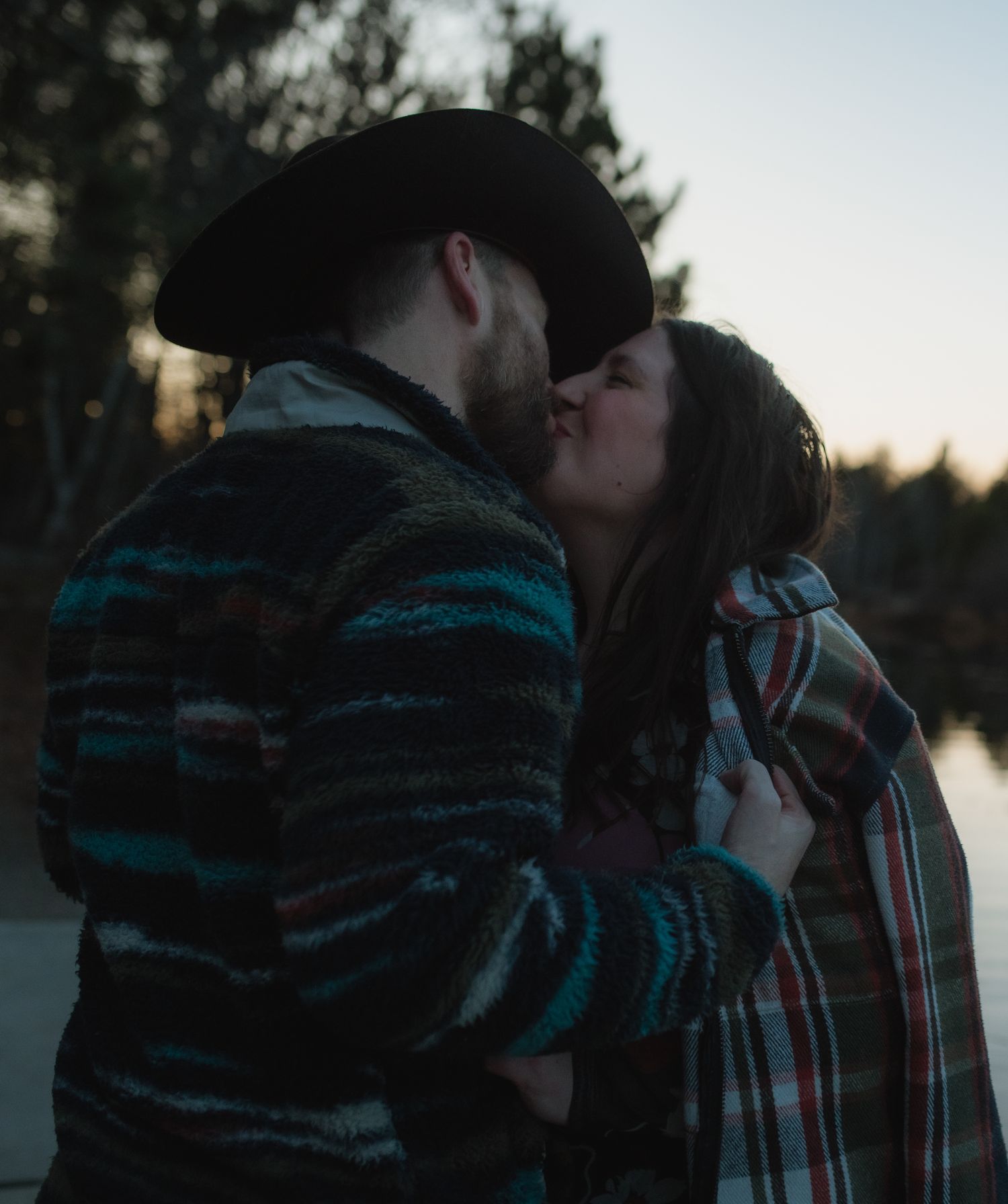 A couple shares an intimate moment at sunset against a wooded backdrop.