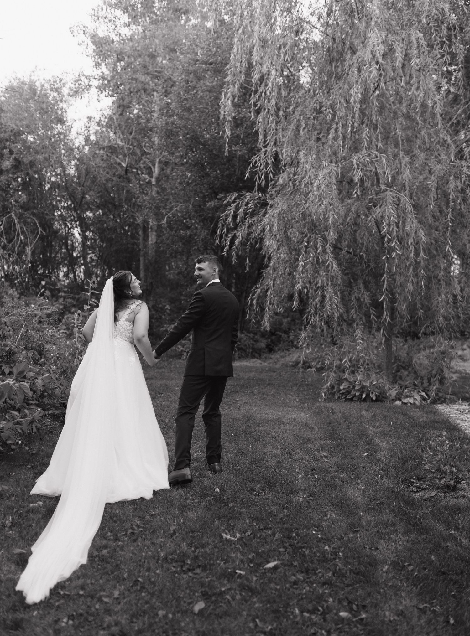 A bride and groom walk together under a weeping willow tree in a romantic black and white wedding photo sequence.