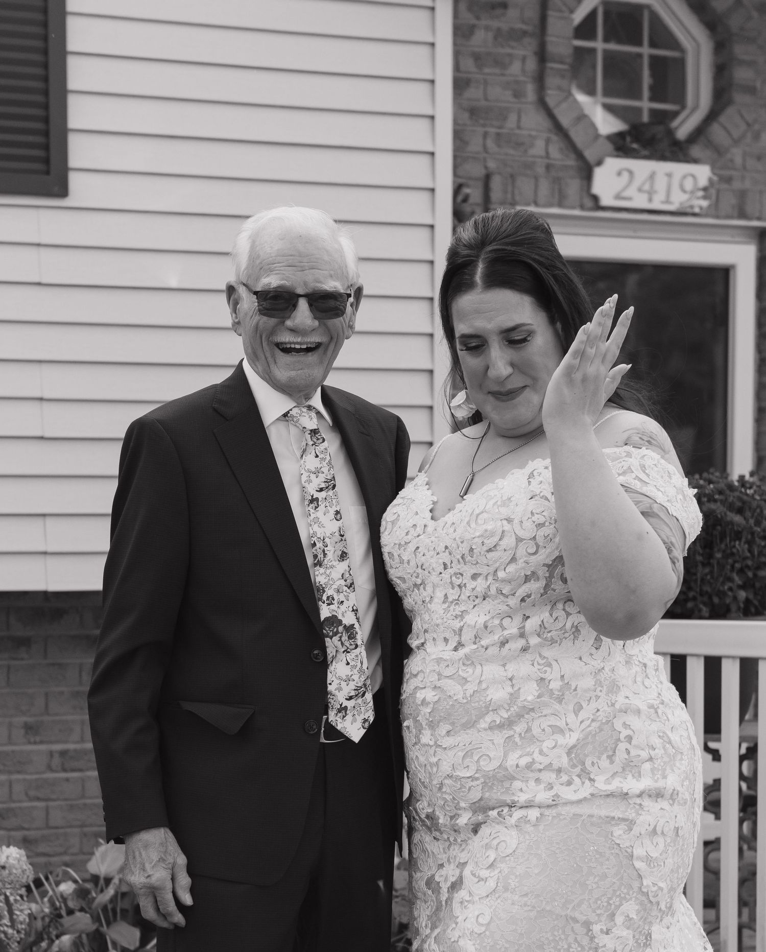 Black and white portrait of two people in formal attire on a house porch.