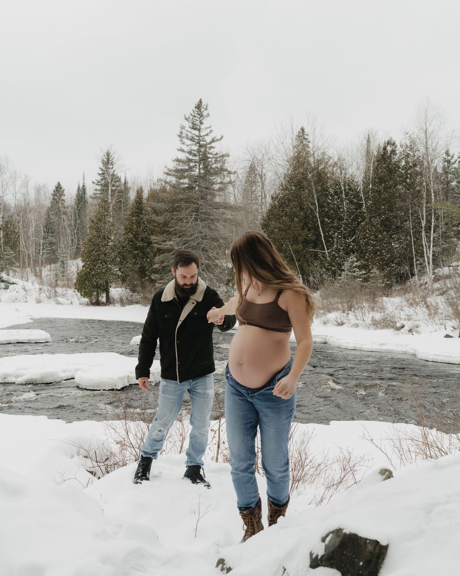 A couple stands together in a snowy landscape during a winter maternity session.