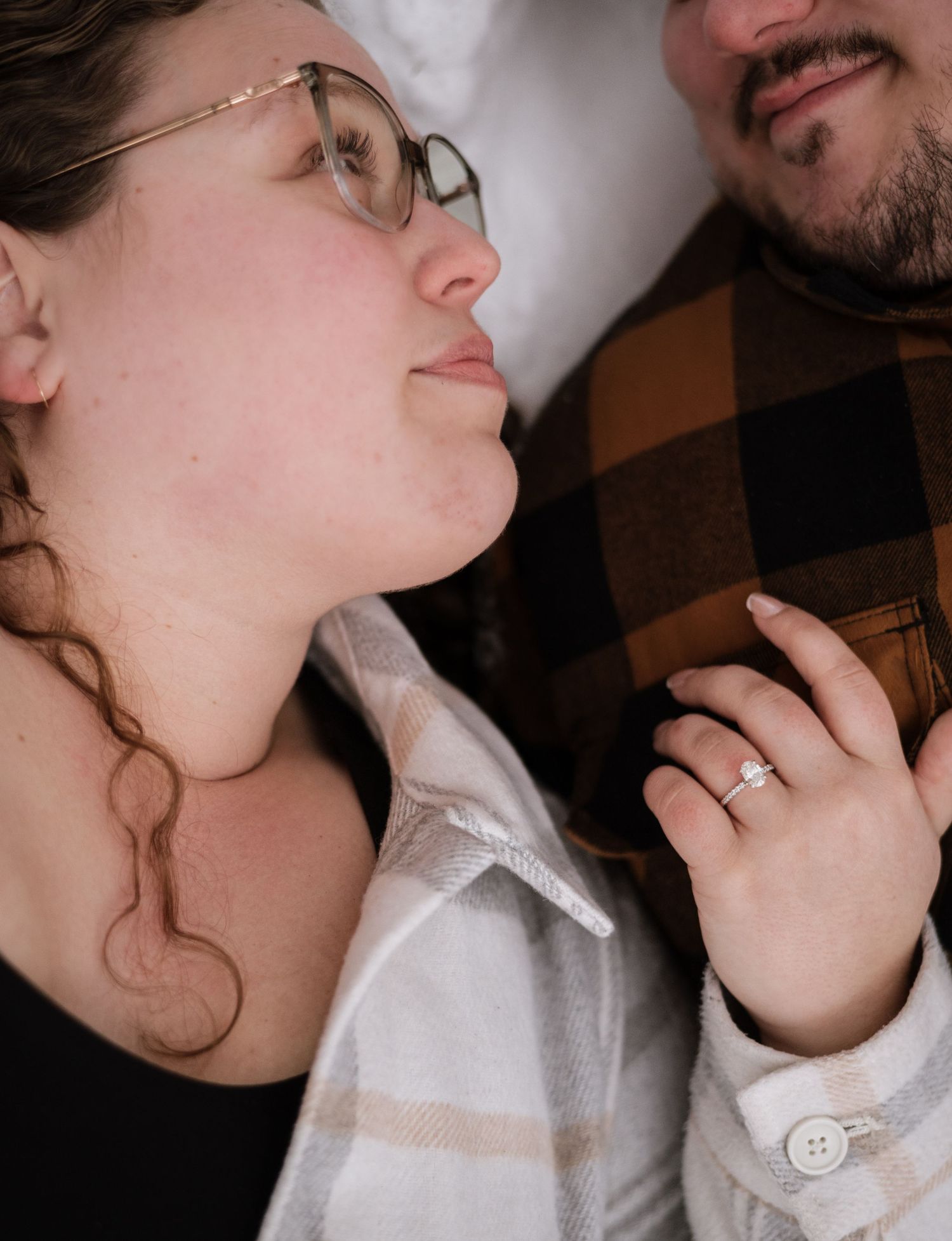 Close-up of engaged woman wearing glasses showing off diamond ring beside smiling man.