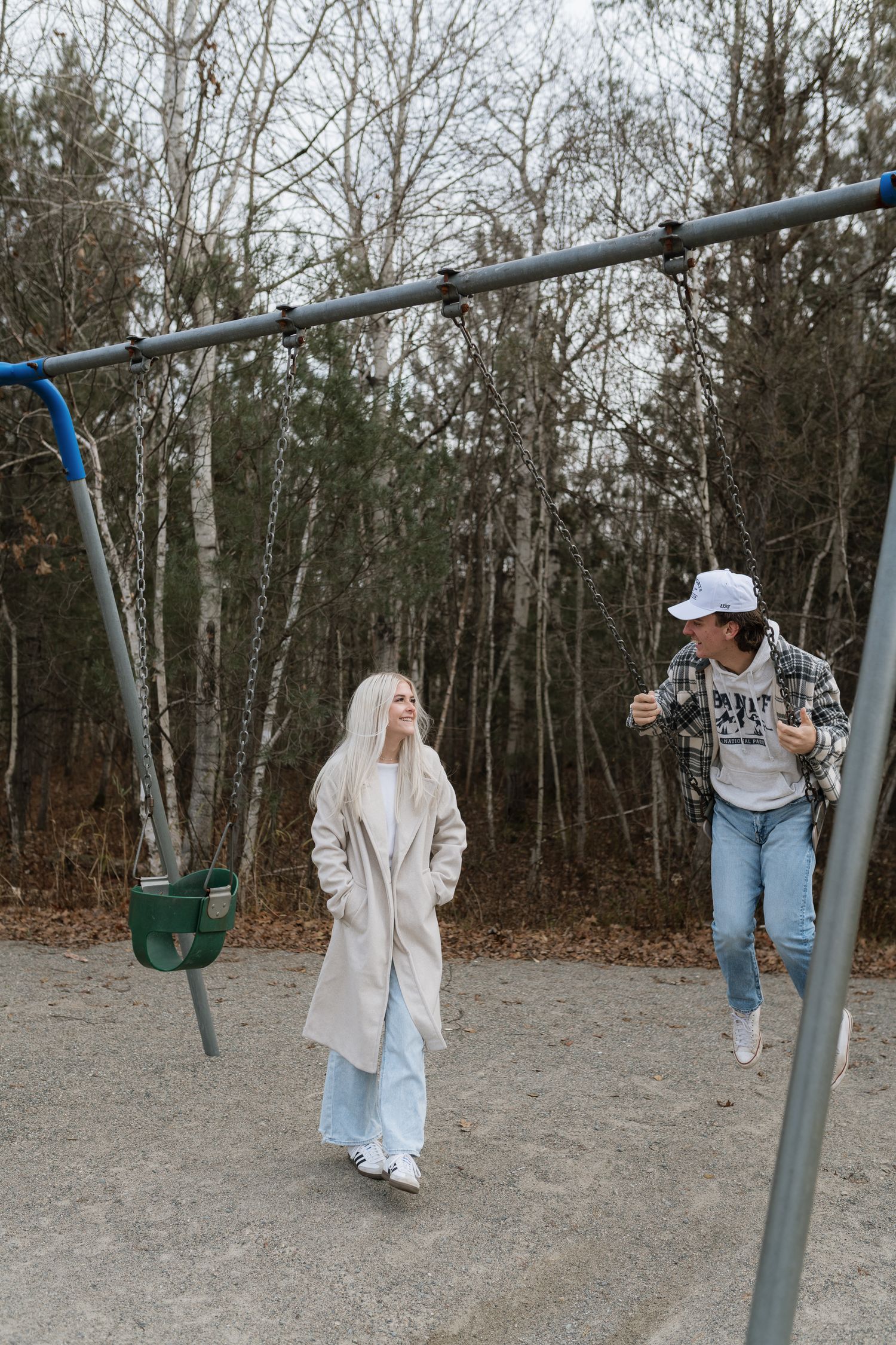 Couple walking at a playground swing set surrounded by bare trees in autumn.