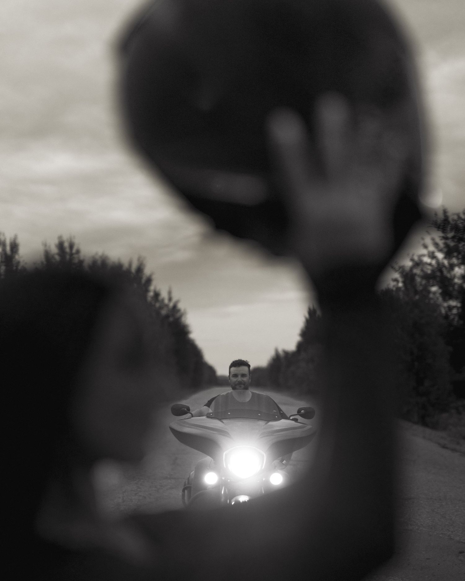 Artistic silhouette photo of a motorcycle with headlight on a dusky road.