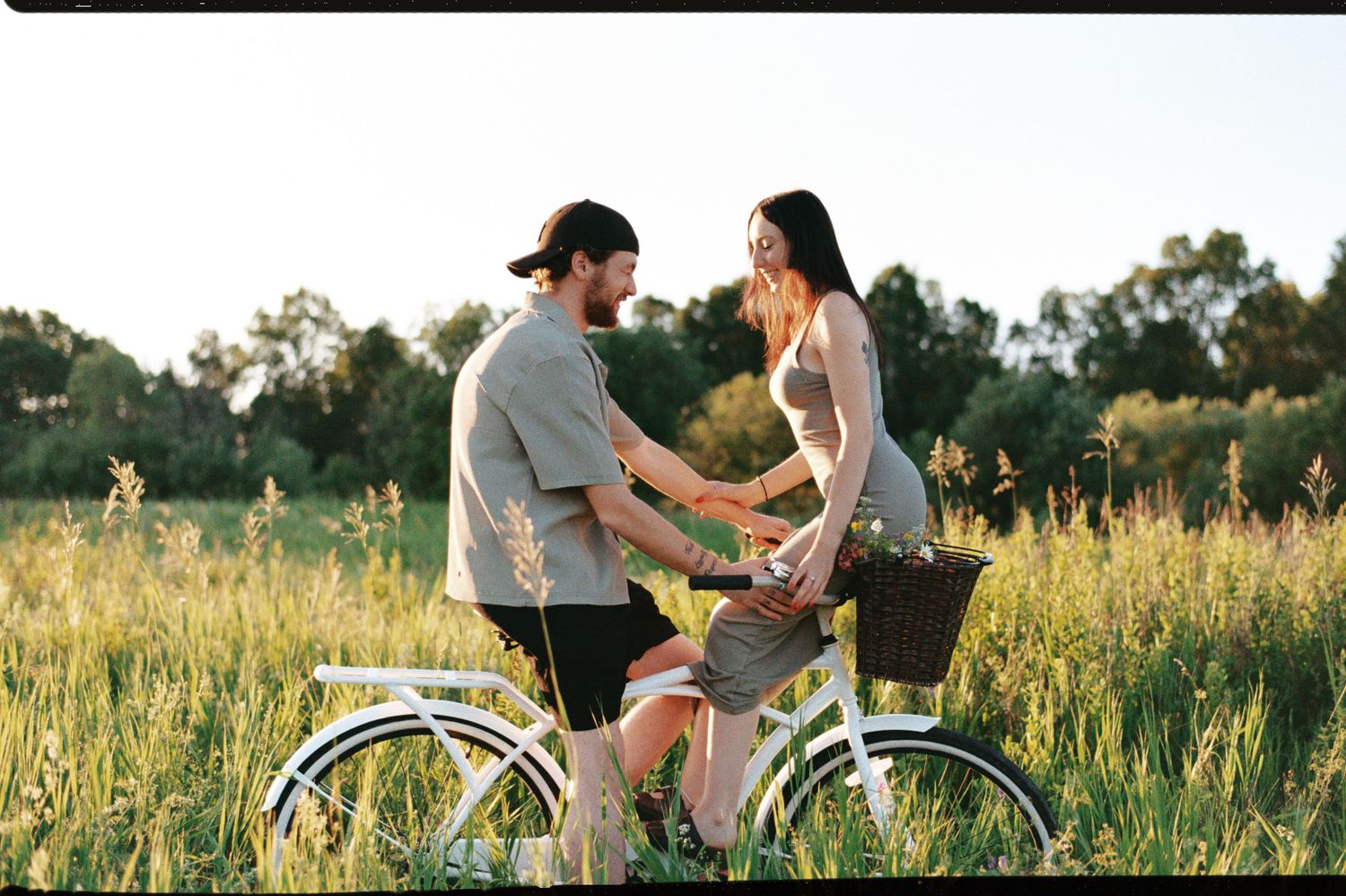 Two people riding bicycles through a golden meadow at sunset with tall grass swaying in the breeze.