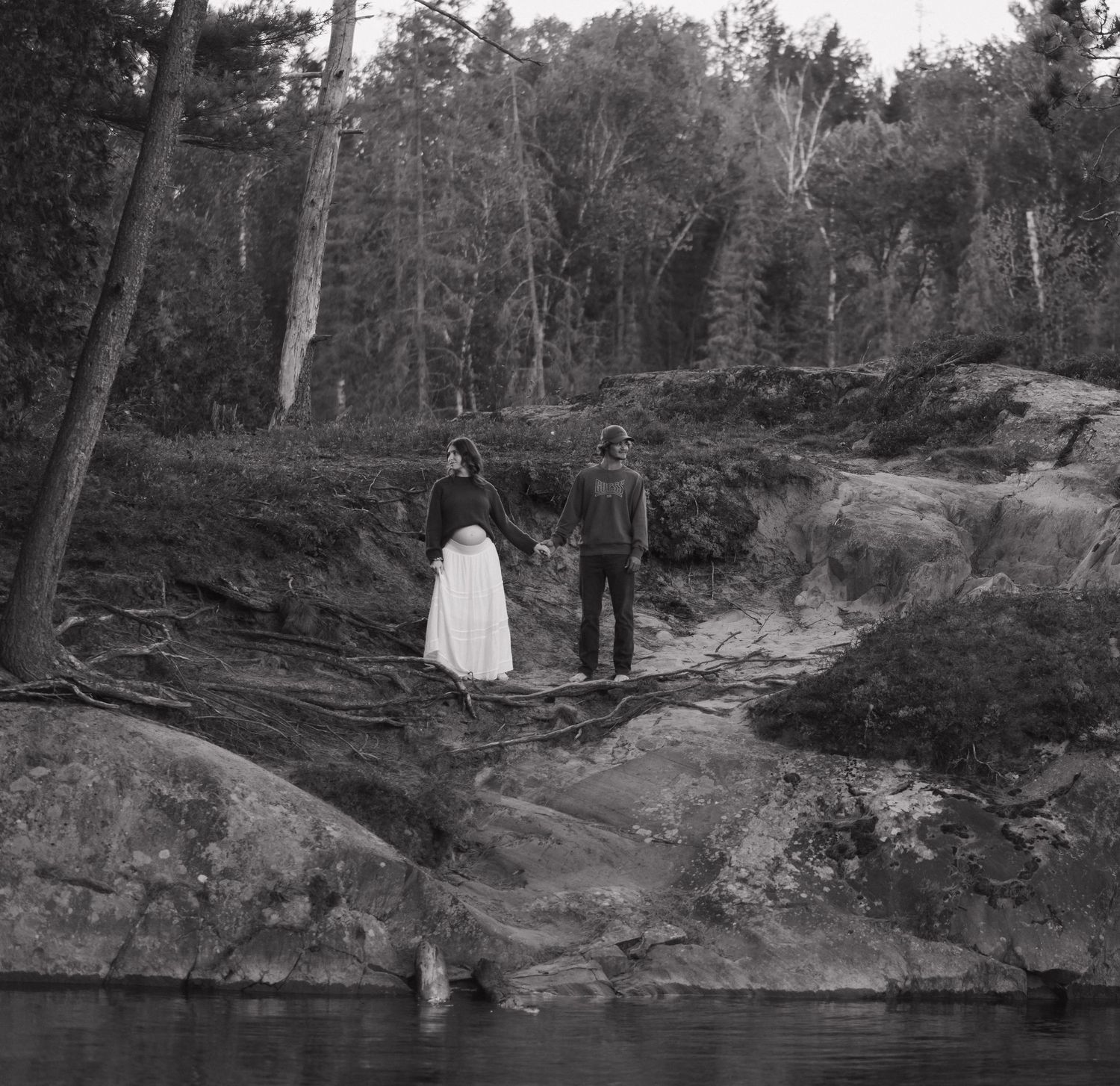 Black and white landscape photo of figures standing on rocky cliffs near a forest.