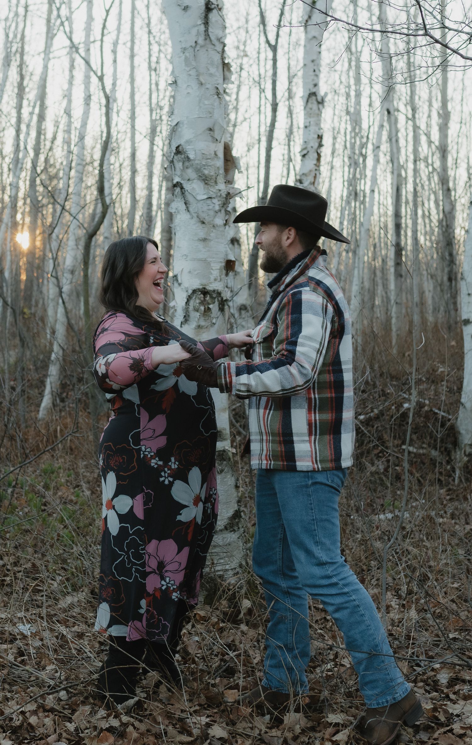 A couple dances together in a birch forest at dusk wearing western and floral attire.