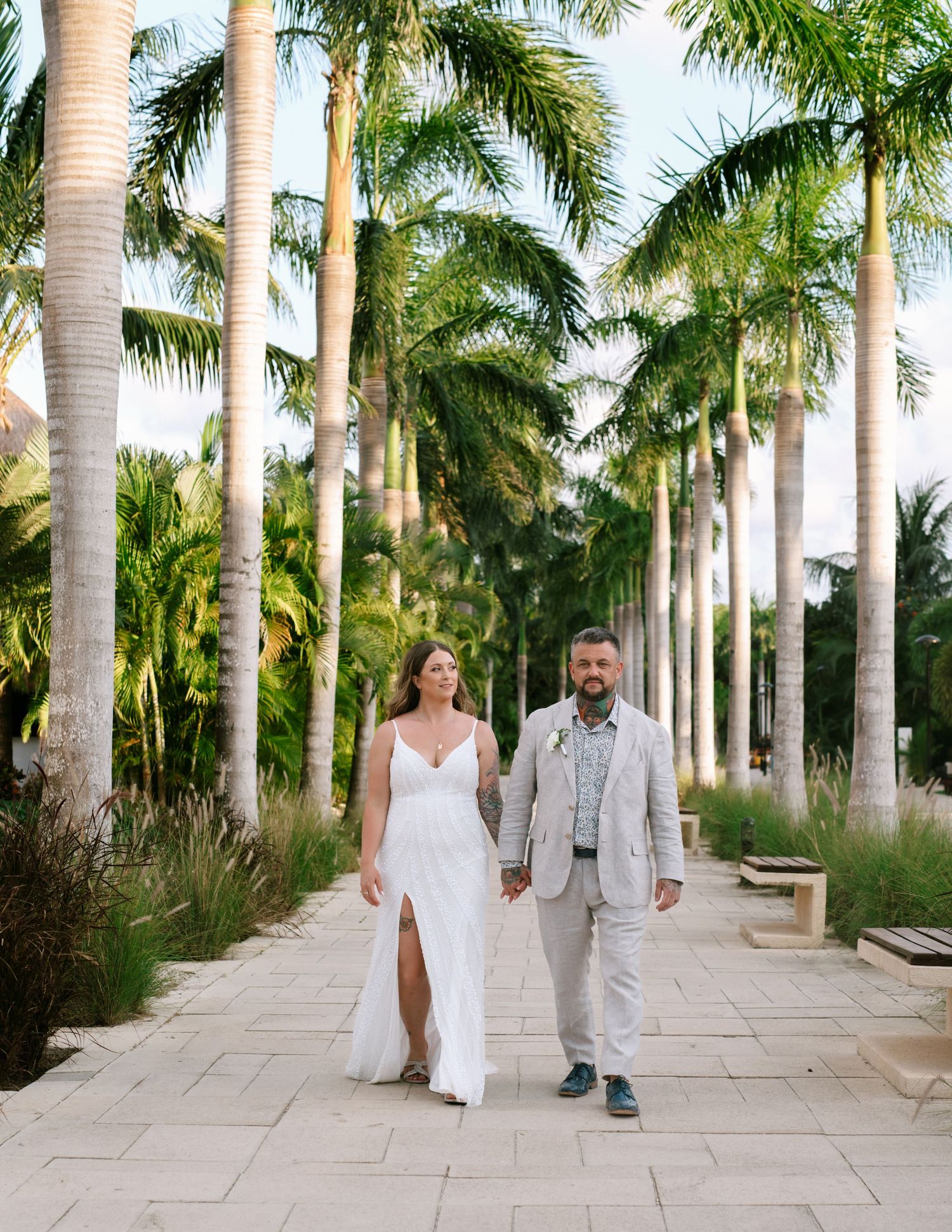 A couple walks along a palm tree-lined pathway in tropical garden setting.