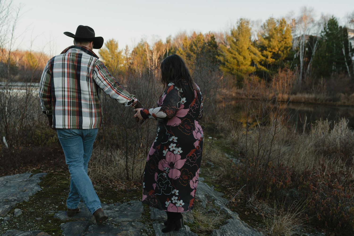 A person in a plaid shirt and cowboy hat walks through an autumn field at sunset with golden light filtering through trees.