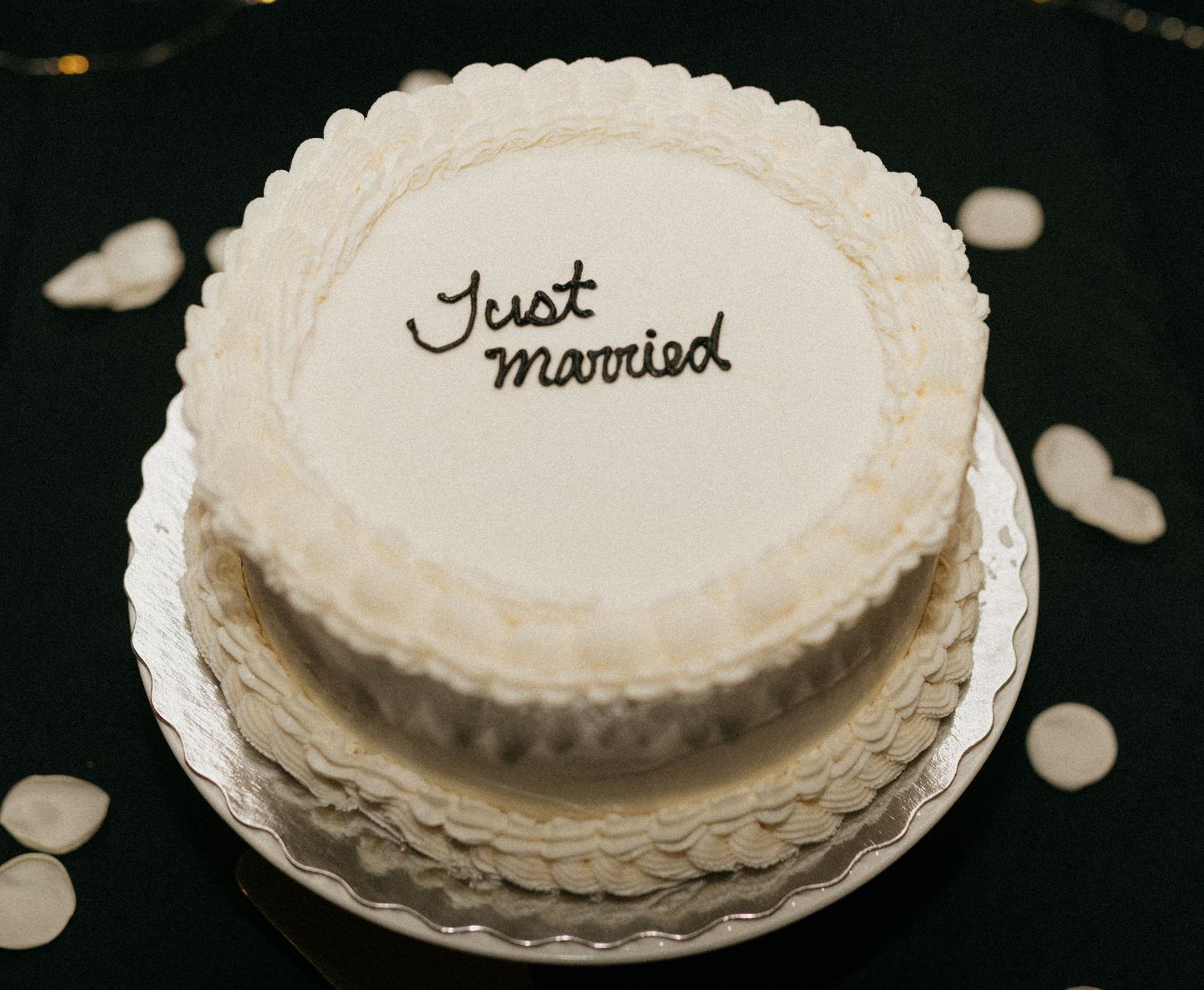 A white frosted wedding cake with delicate piped details on a dark background.