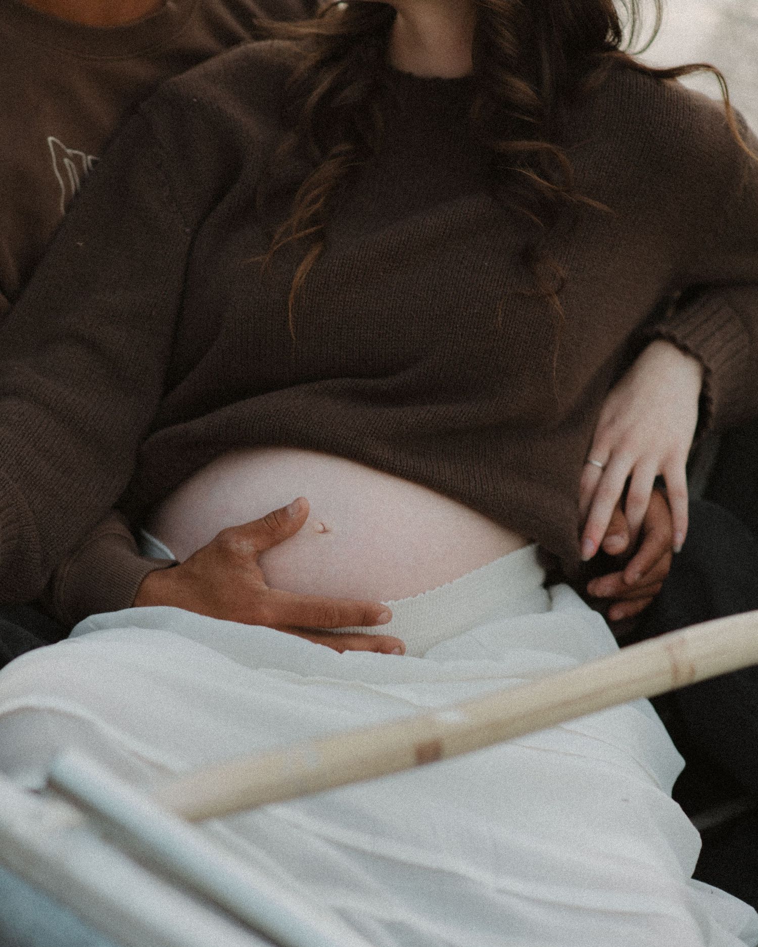 Maternity photo showing gentle hands resting on a pregnant belly covered with white fabric.