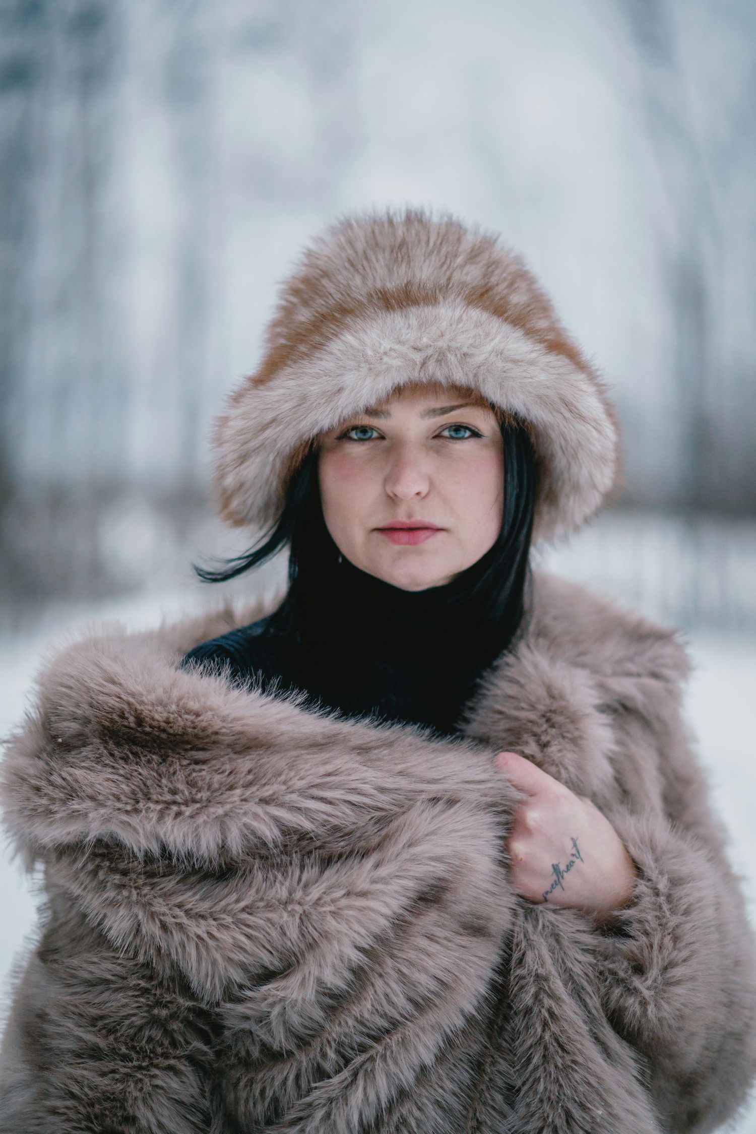 A person wearing a cozy fur-trimmed winter coat poses against a snowy winter forest backdrop.