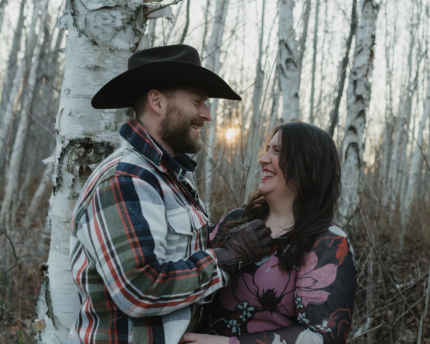A romantic couple in western attire embraces in a snowy aspen forest during a winter photoshoot.