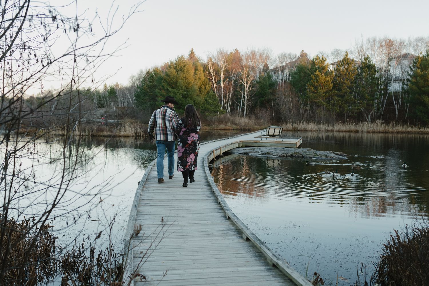 People walk along a wooden boardwalk path over wetlands surrounded by autumn trees and still waters.