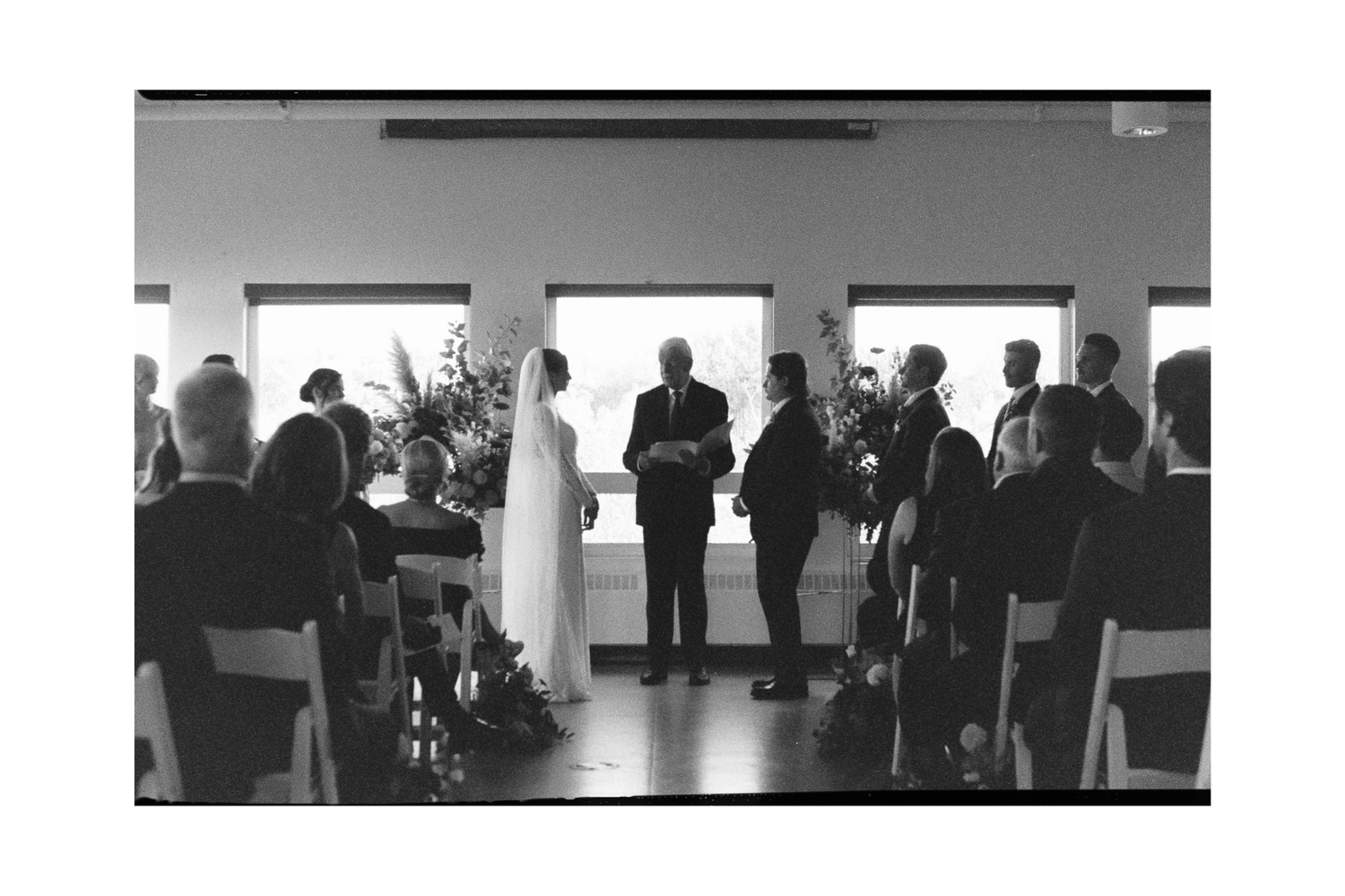 Silhouettes of people seated in rows during a presentation or meeting in a modern room with large windows.
