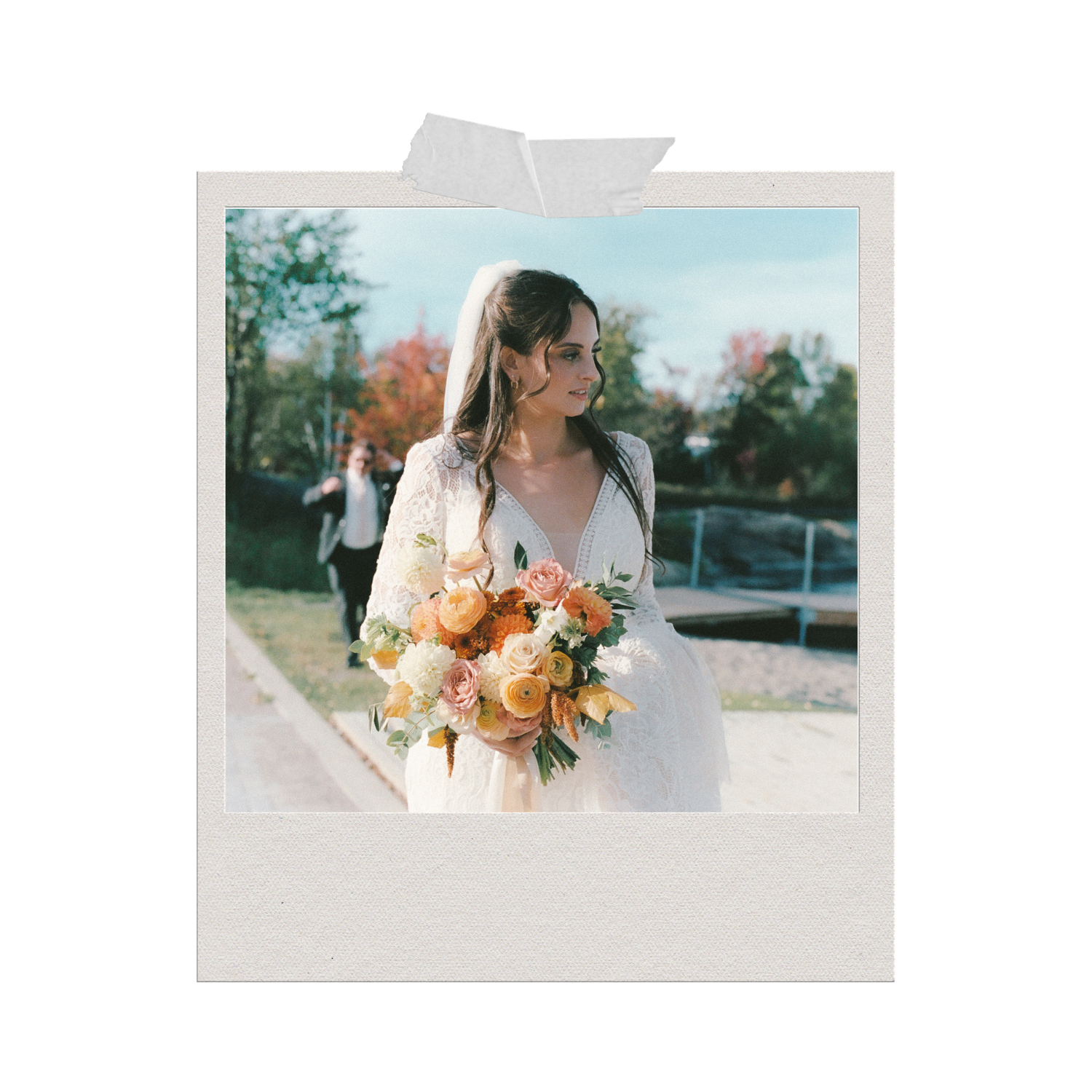 Bride in white gown holding orange and white floral bouquet outdoors on sunny day with autumn trees.