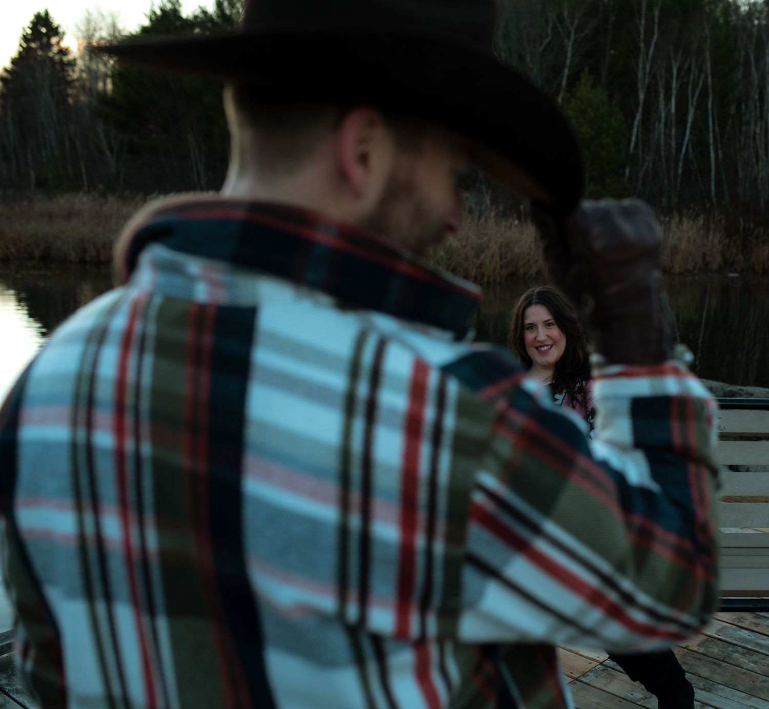 People in plaid shirts walk together on a path through trees and greenery at sunset.