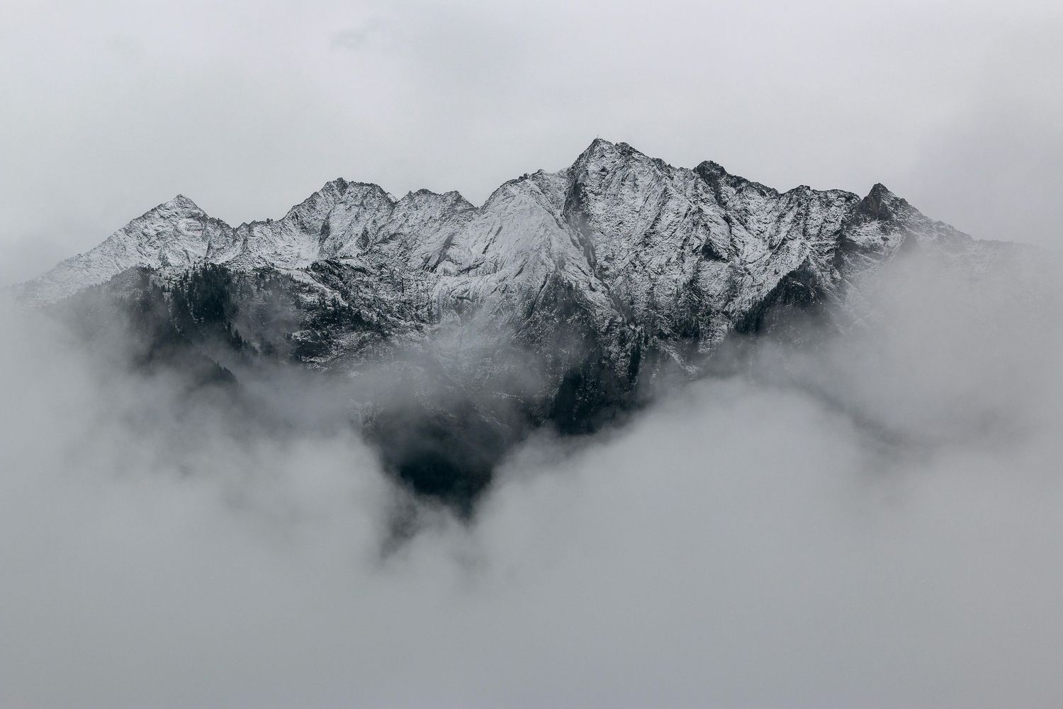 Dramatic mountain peaks shrouded in misty clouds create a moody panoramic landscape view.
